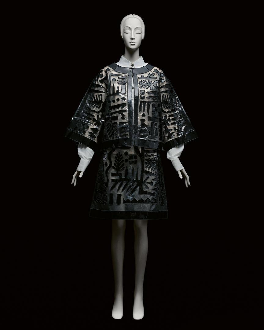 A black dress fitted on a full body white mannequin in dramatic lighting against a pitch black background.