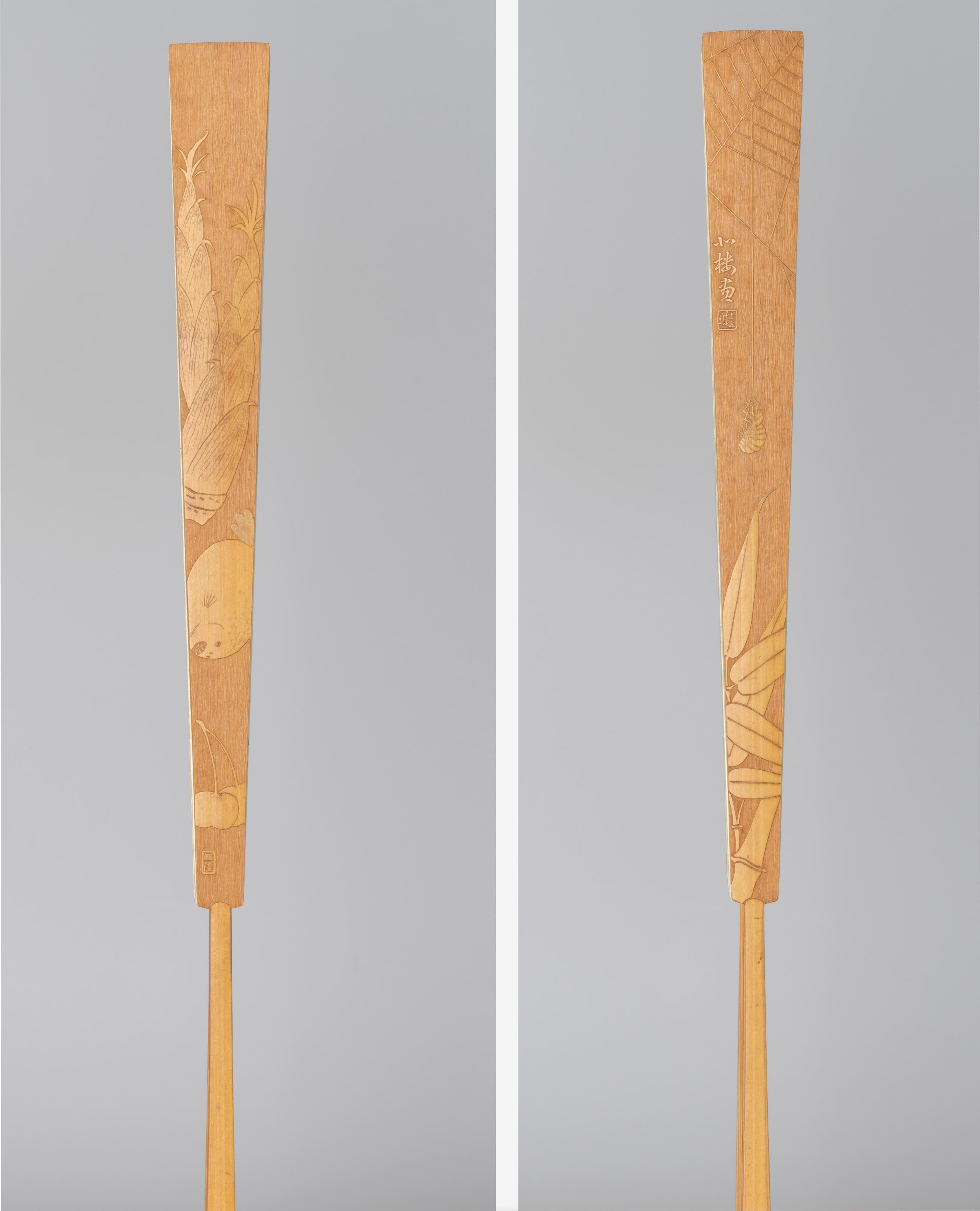 Wooden side of a fan with intricate engravings of bamboo and moon motifs set against a light grey background