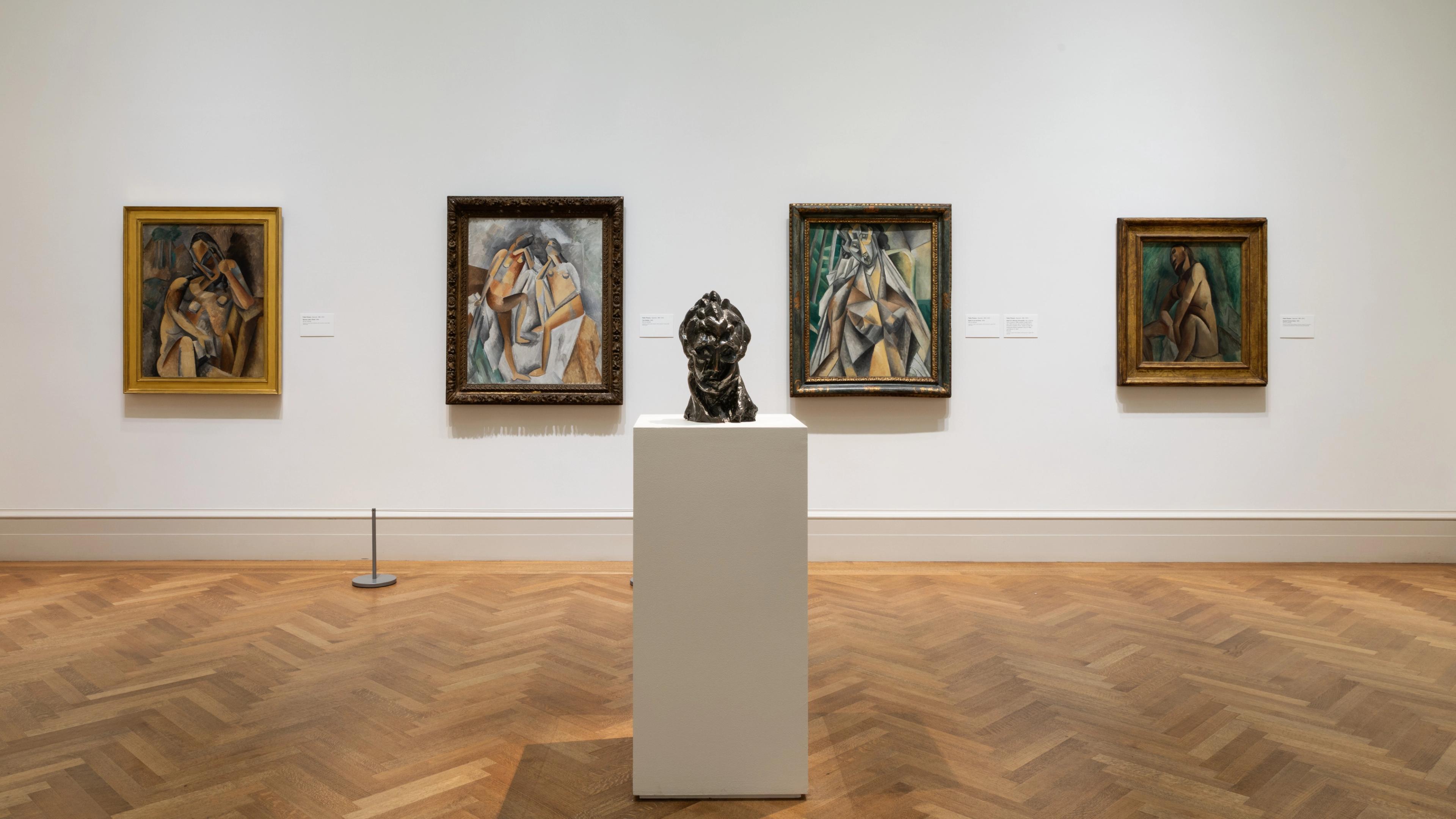 Four Cubist paintings and a sculpture of a bust against a gallery wall