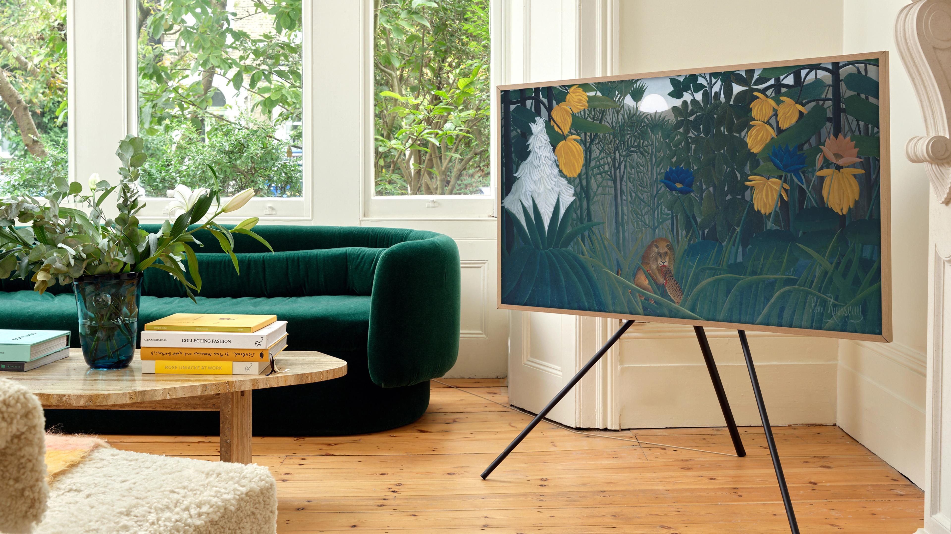 A stylish living room features a framed art TV displaying a vibrant jungle scene, complemented by a plush green sofa and plants.