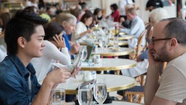 Two Museum visitors sit at a table in the American Wing Cafe in The Met, talking over drinks.