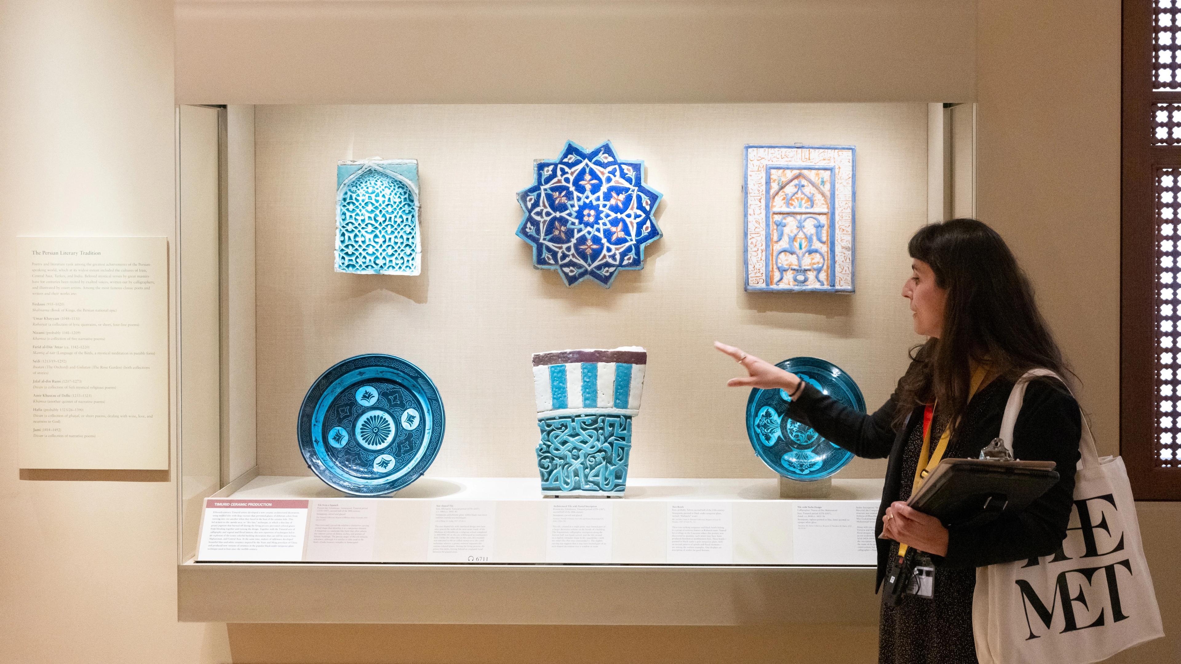 Someone gives a tour in front of a case of blue objects at The Met