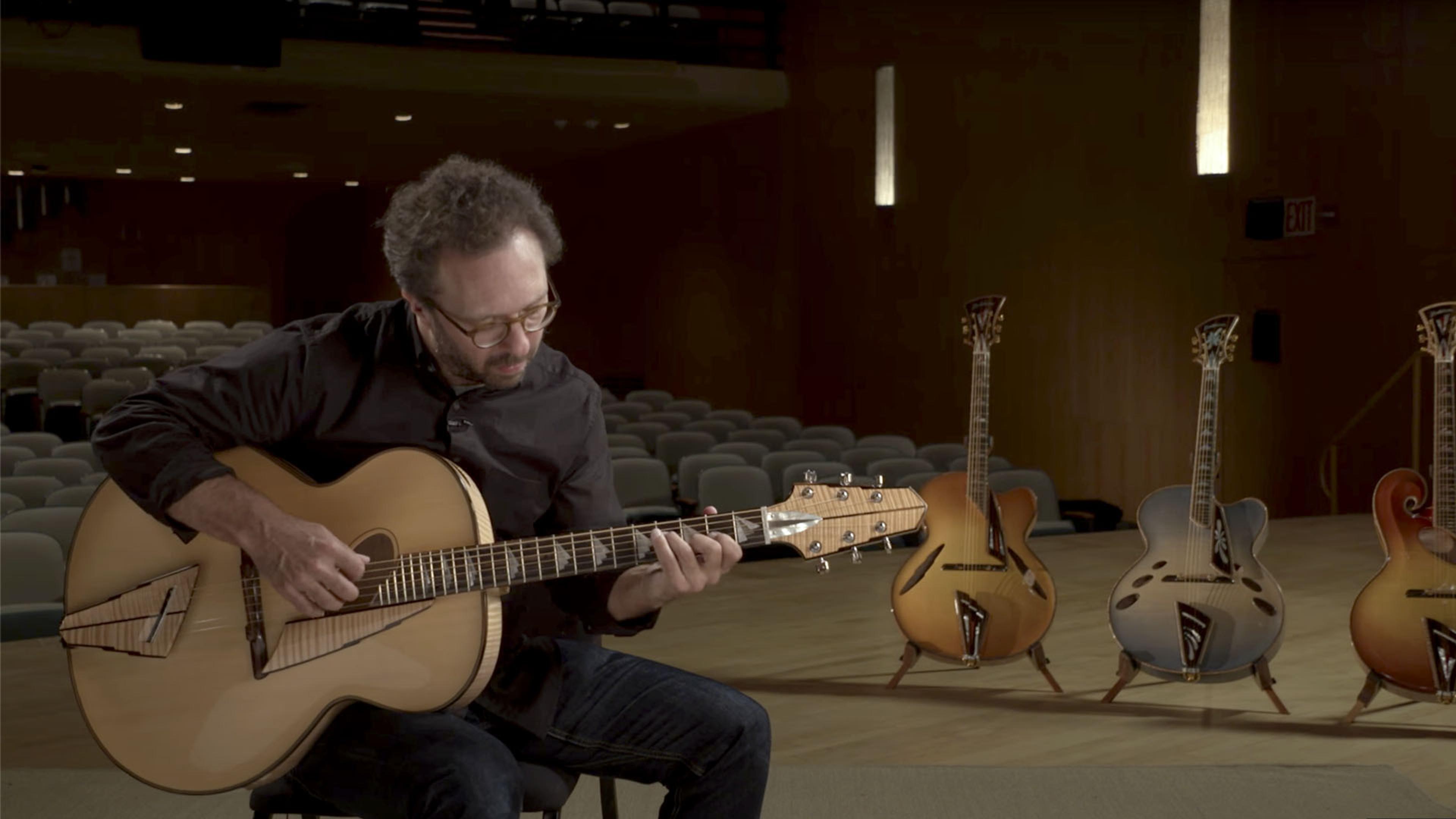 Guitarist and composer Anthony Wilson plays a guitar on a stage with three additional guitars in the background