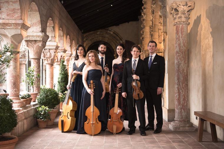 The six members of Sonnambula pose in one of the cloisters at The Met Cloisters holding their instruments (violins and viols)