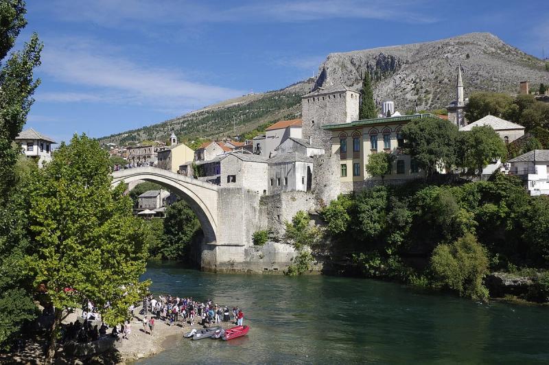 Stari Most arching over the green Neretva river, with the old town and mountains behind