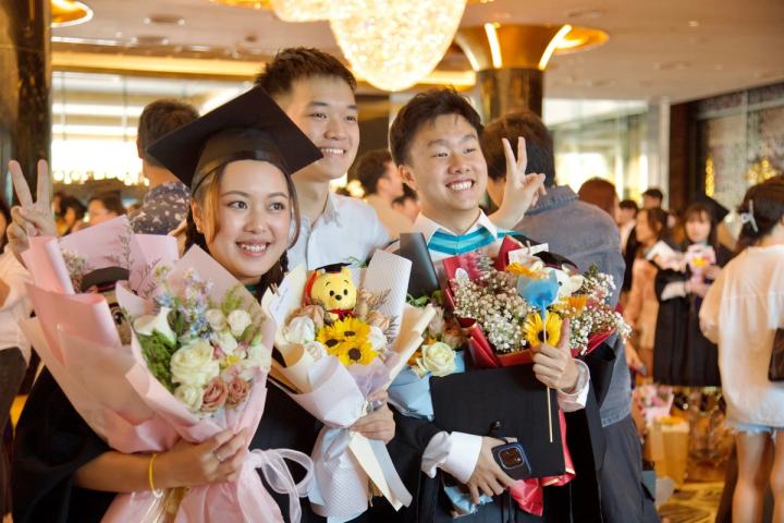 Students celebrate graduation by tossing caps indoors. Joyous academic milestone.