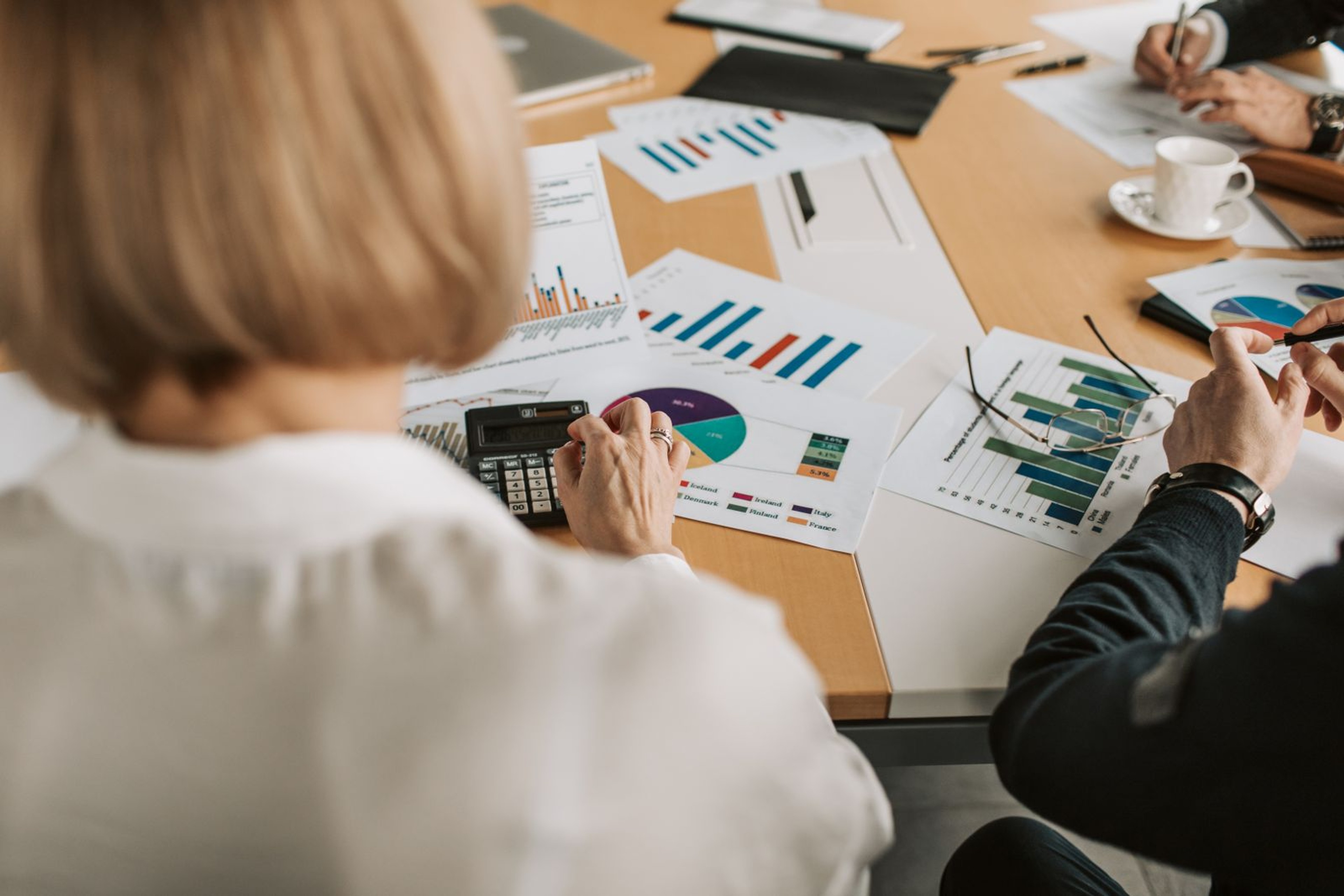 Two people reviewing marketing budget charts with a calculator on a meeting table