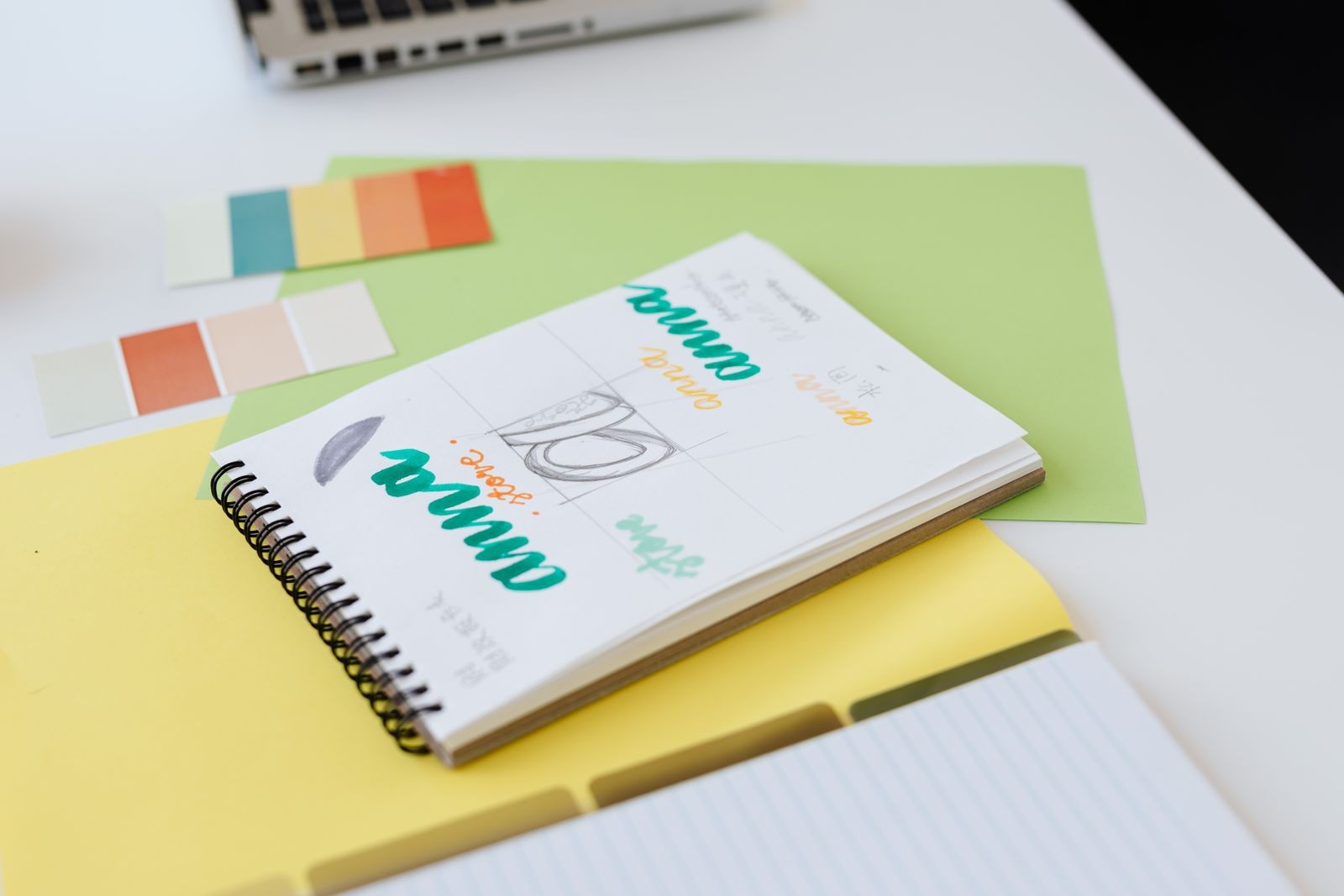 Notebook of hand-drawn brand identity sketches next to color swatches and paint chips
