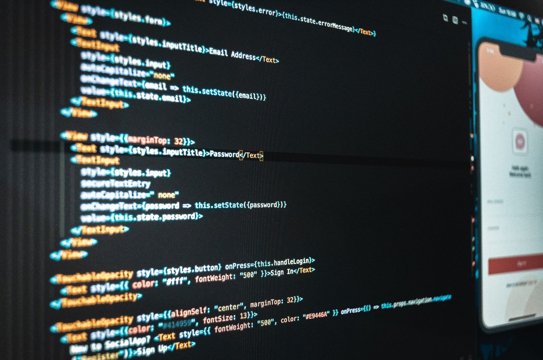 Close-up of application code and a mobile app preview panel on a laptop screen