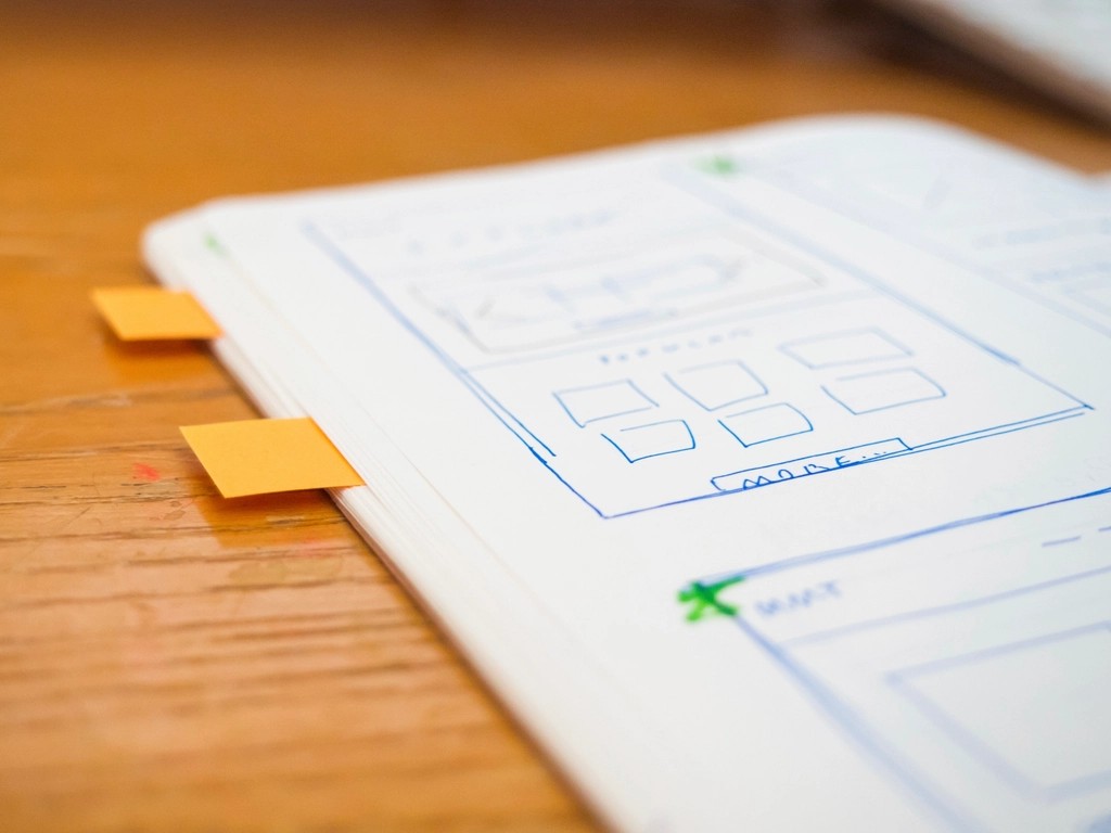 Carnet ouvert sur des wireframes dessines au stylo, deux marque-pages orange sur la tranche.