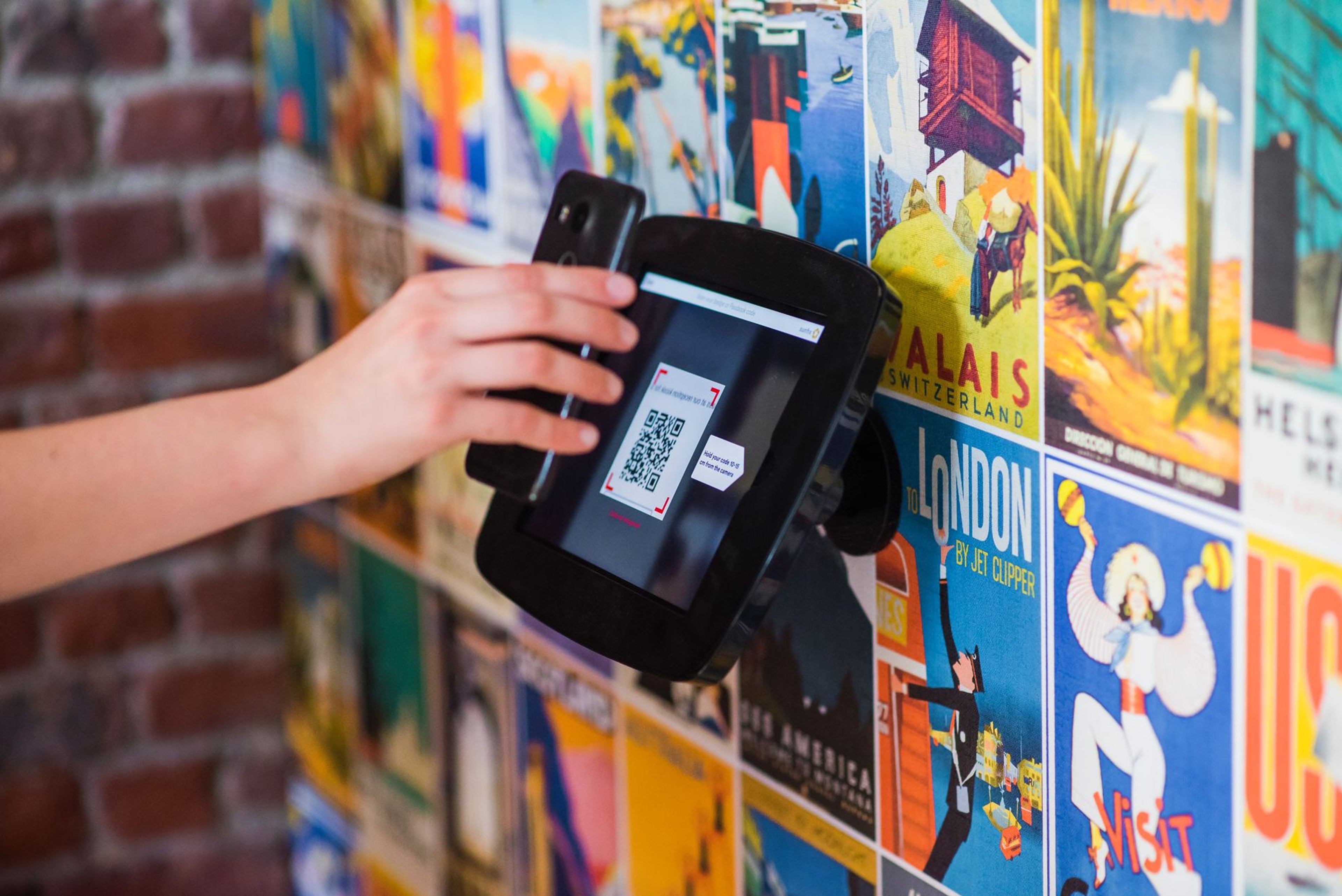 Hand scanning a QR code payment terminal mounted on a wall