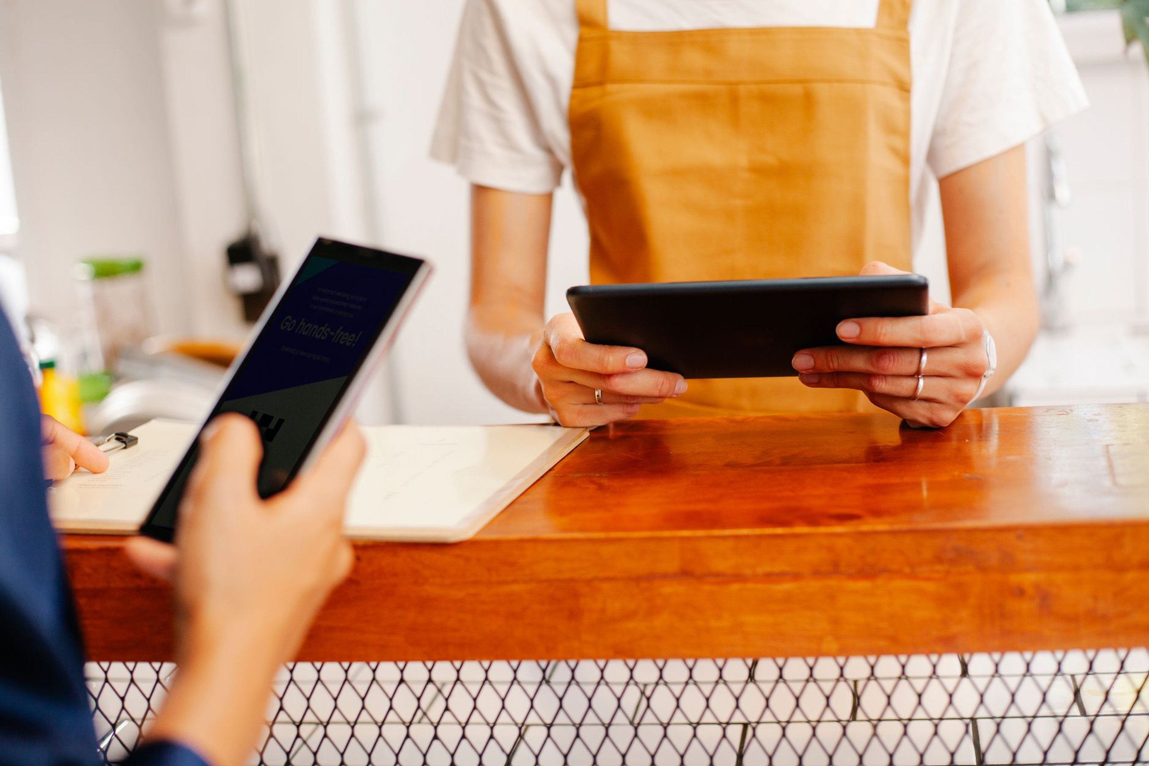 Cafe staff member holding a tablet point-of-sale device while a customer checks a phone at the counter