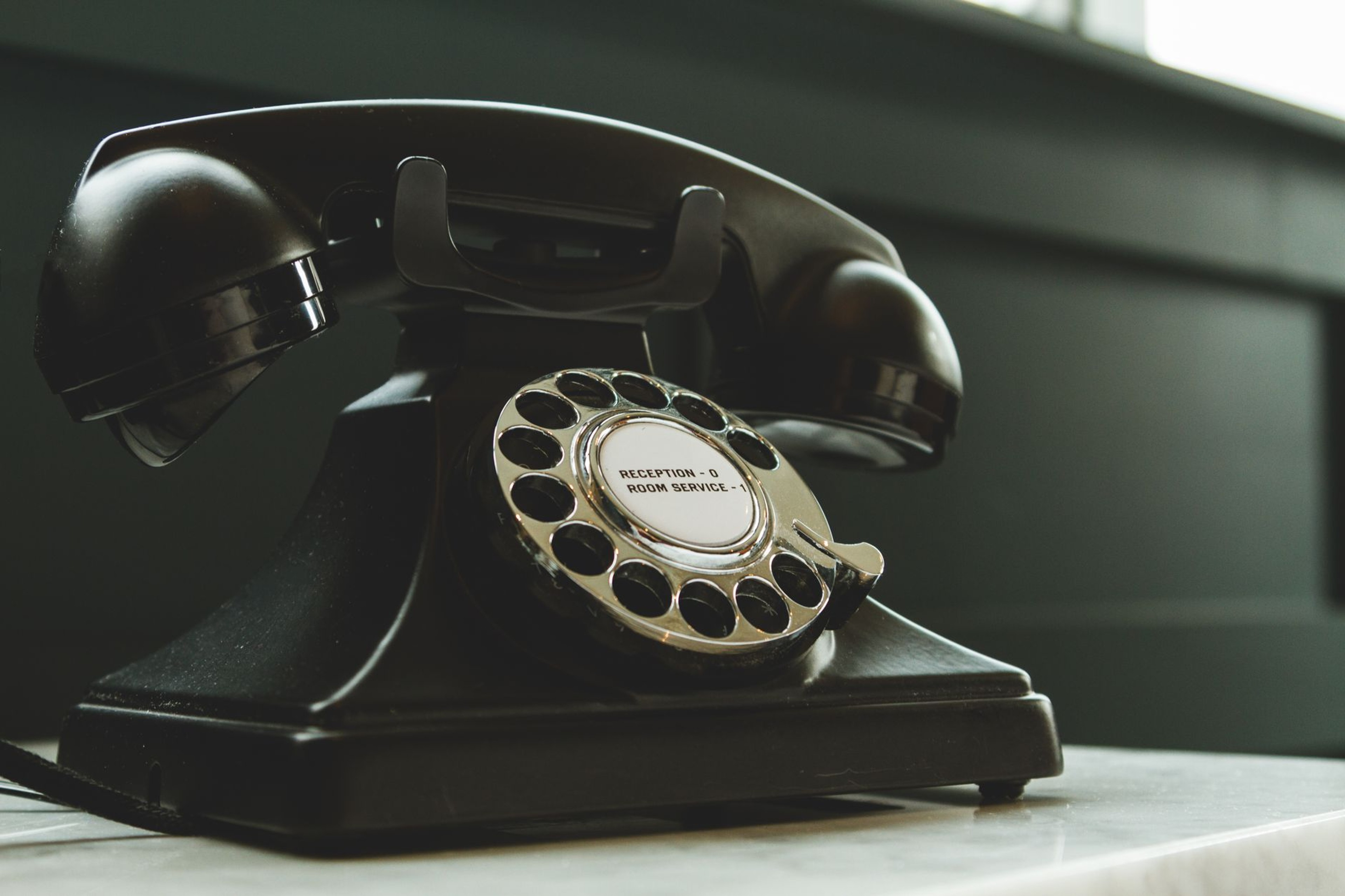 Vintage black rotary telephone labeled reception and room service on a hotel desk