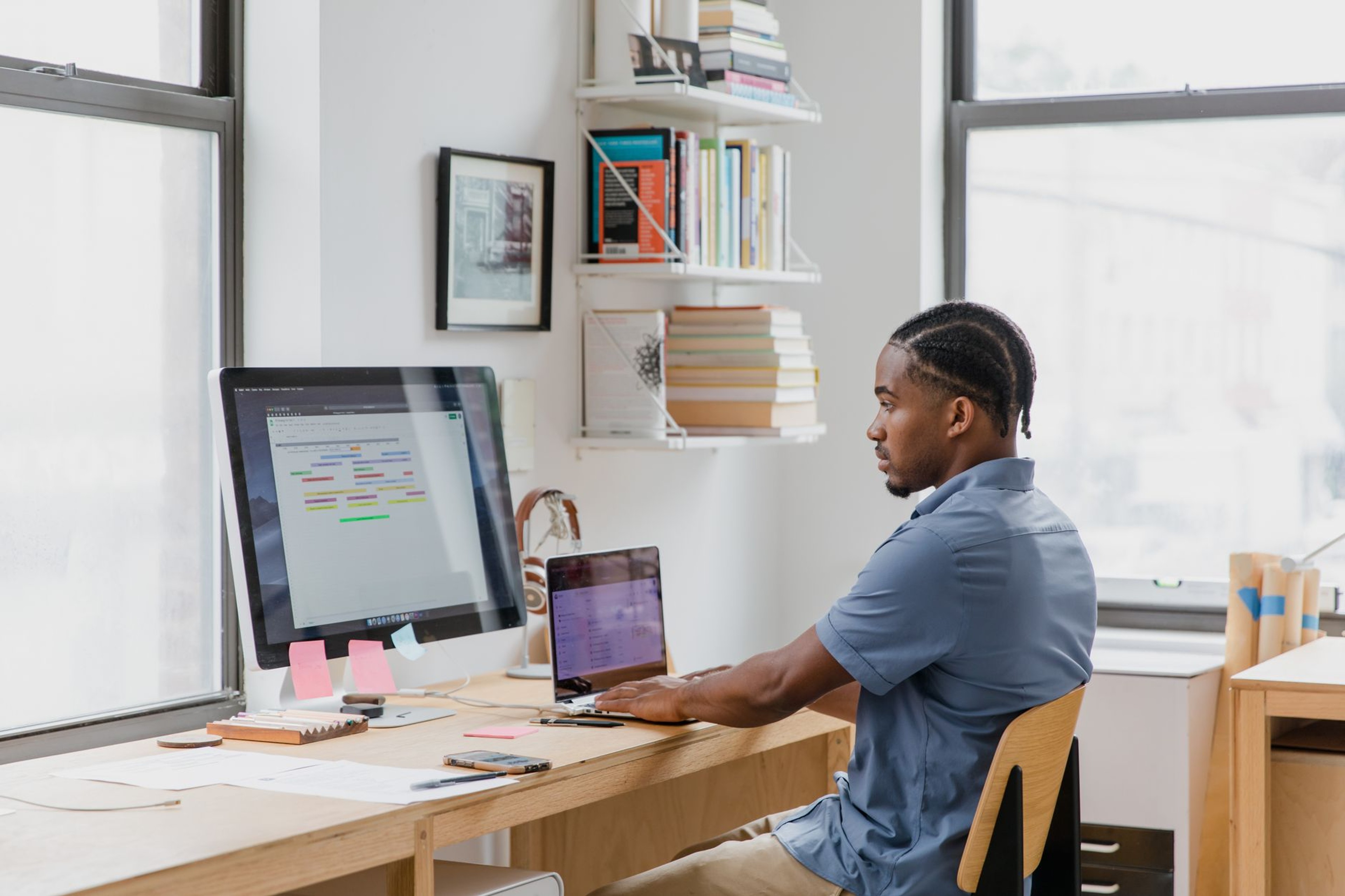 Person working at a desk with a desktop monitor and a laptop side by side
