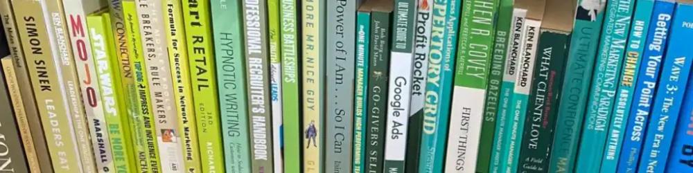 Banner image of a bookshelf with books in a gold colour on the left, transitioning through green to blue on the right. DeskSpace business books.
