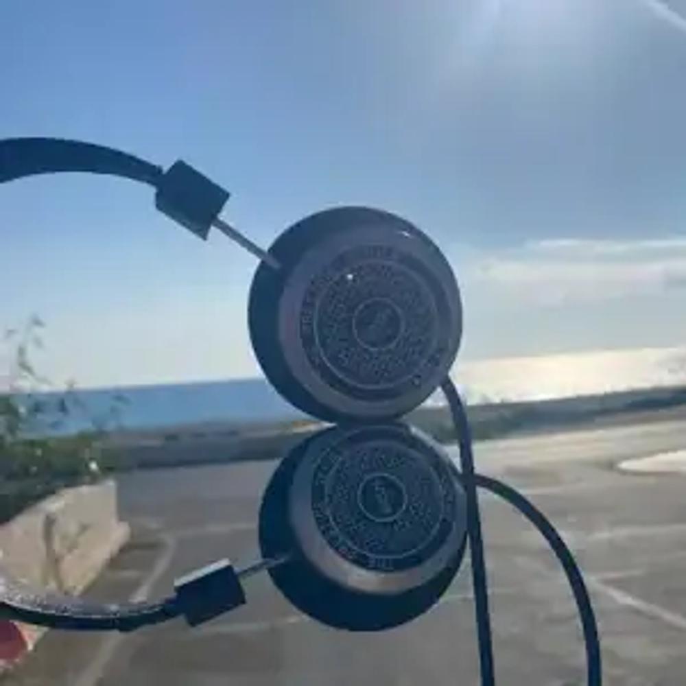 The headphones are held to the left of the shot - at 90 degrees with a sea background.