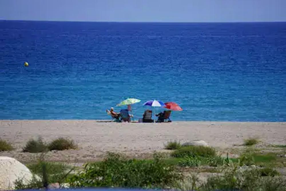 Blue sky, blue sea and 3 coloured beach umbrellas.