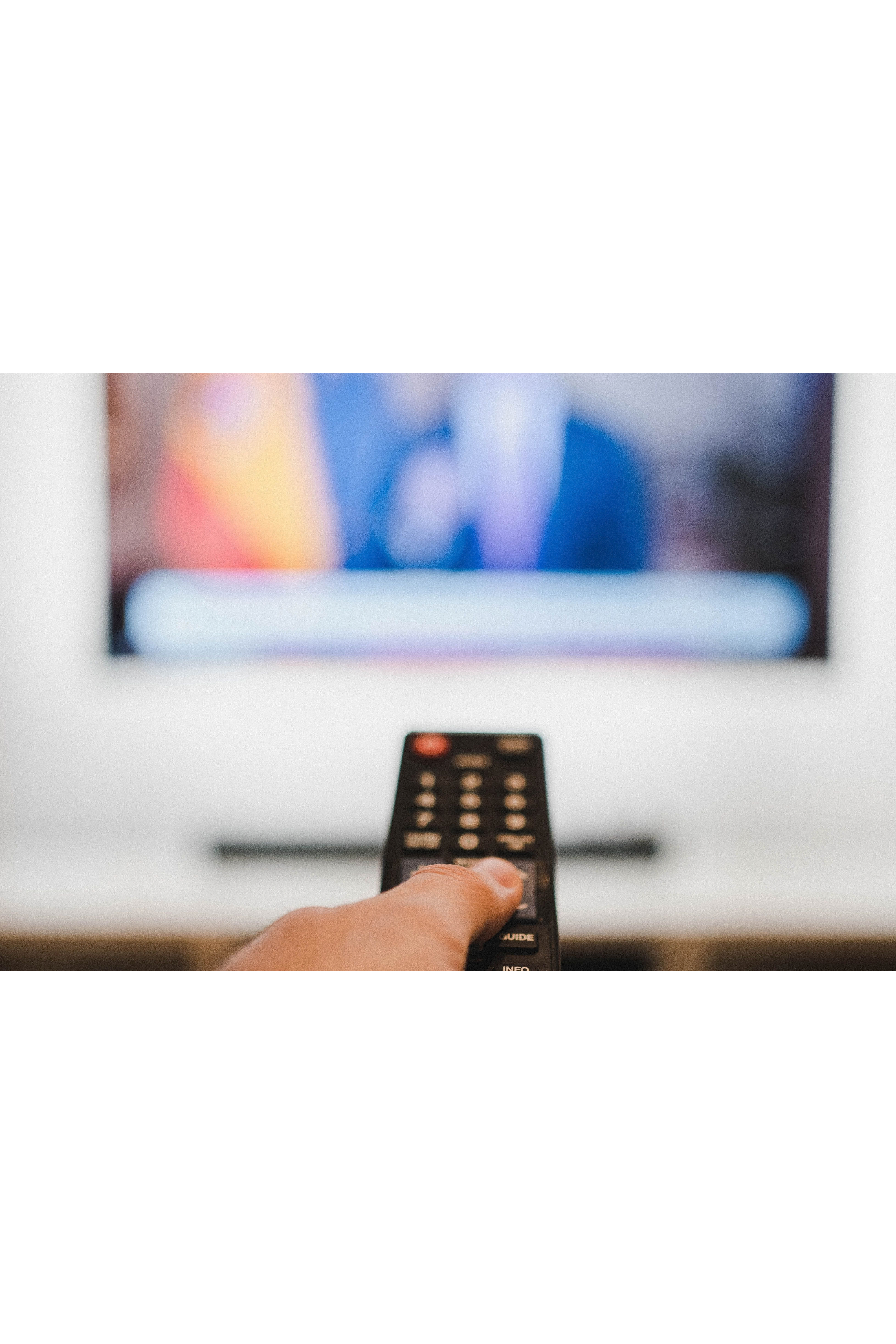  Close-up of a hand holding a remote control towards a TV screen indoors.