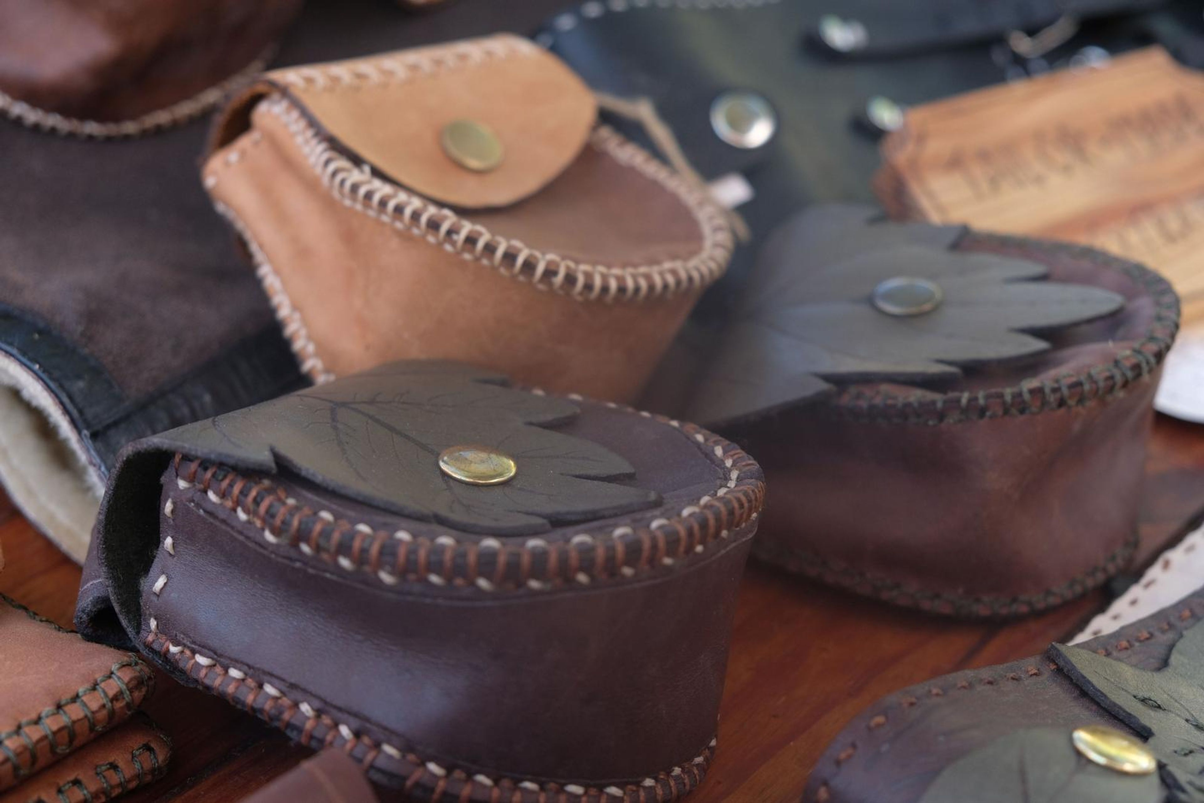 Stack of handmade leather pouches in tan, brown and leaf green with brass studs