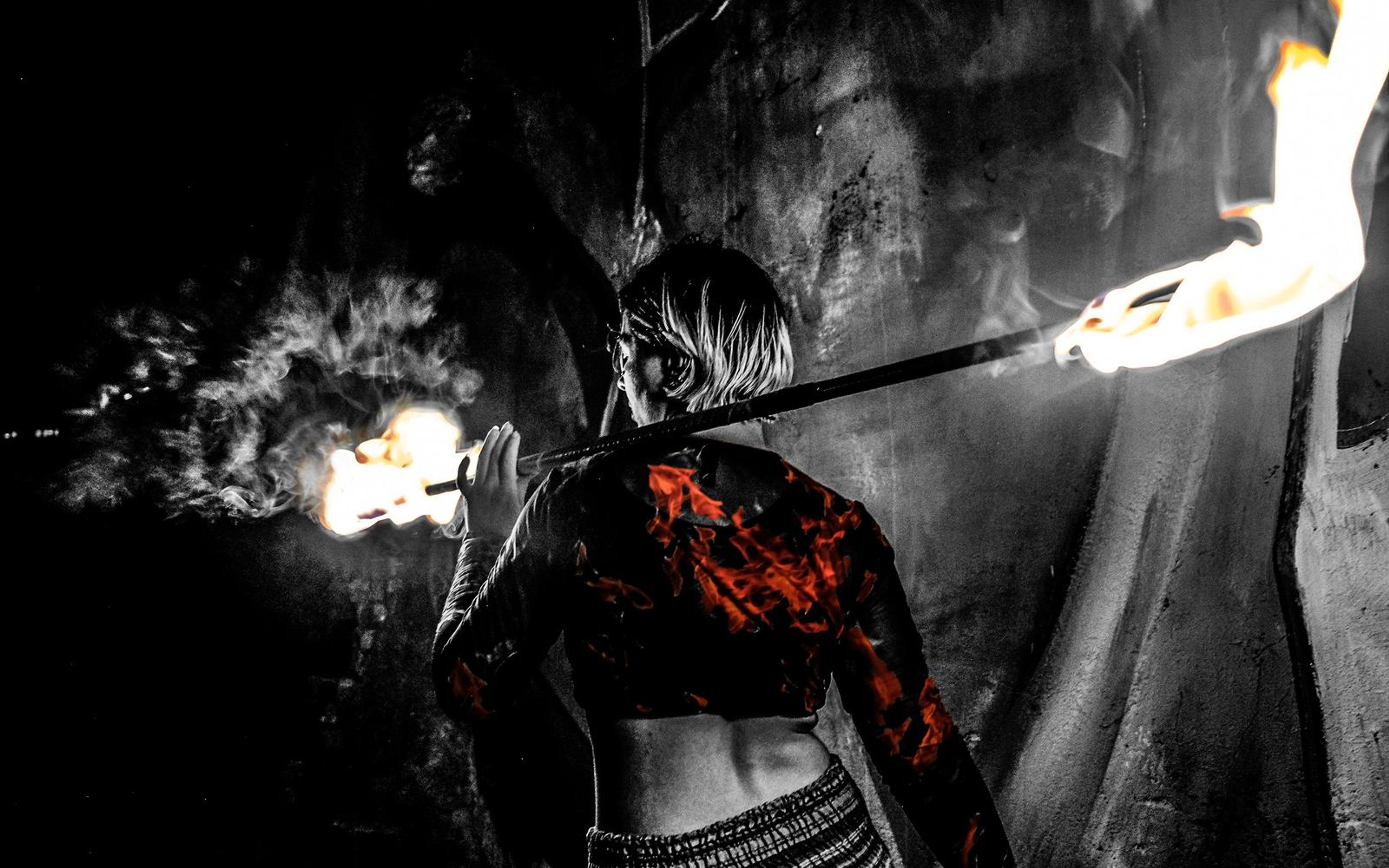Black and white version of the performer from behind with a fire staff across the shoulders and smoke