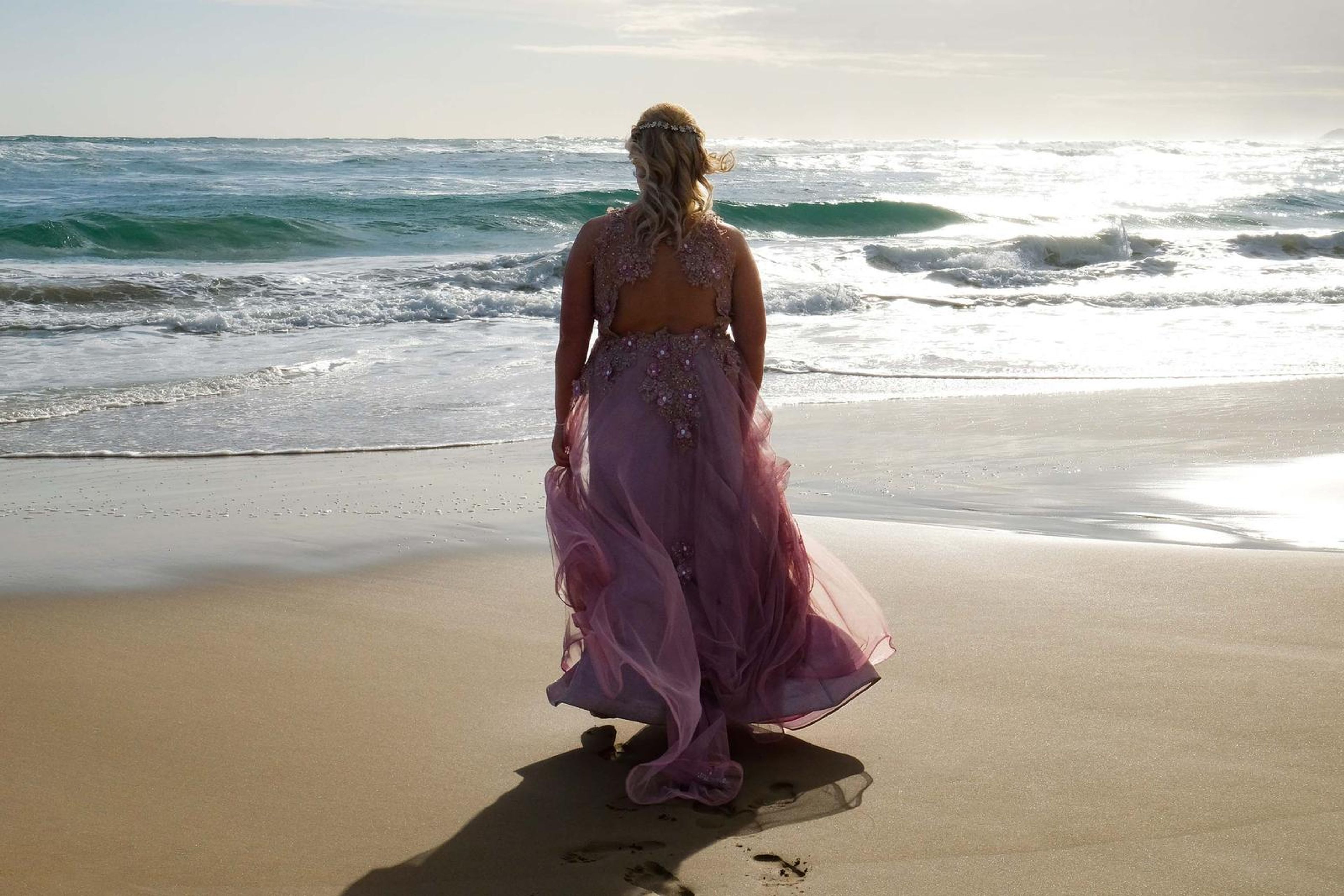 Back view with the gown trailing across the wet sand