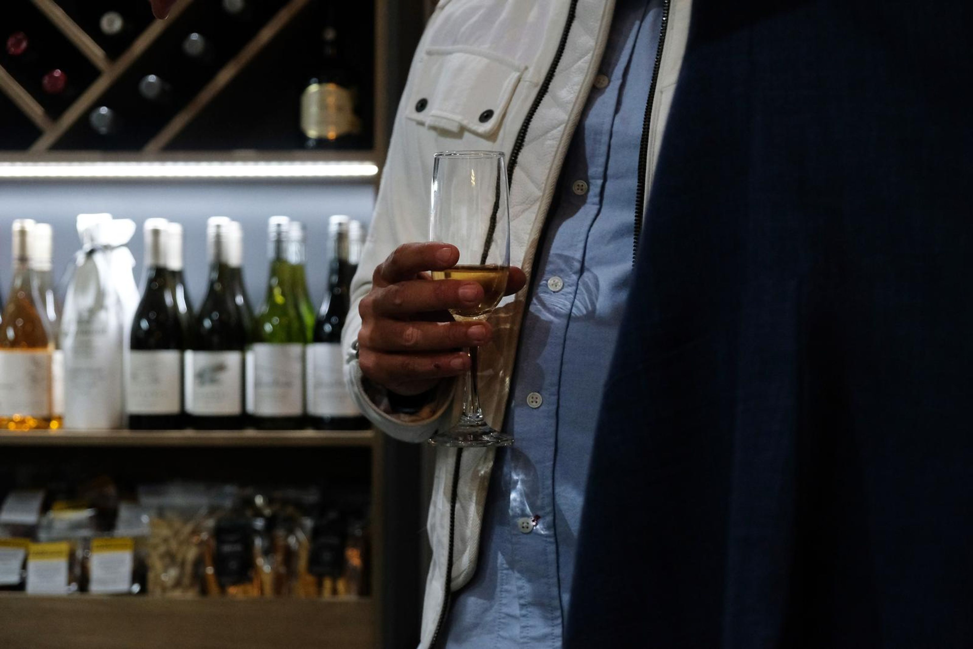 Guest holding a glass of wine in front of the wine shelves