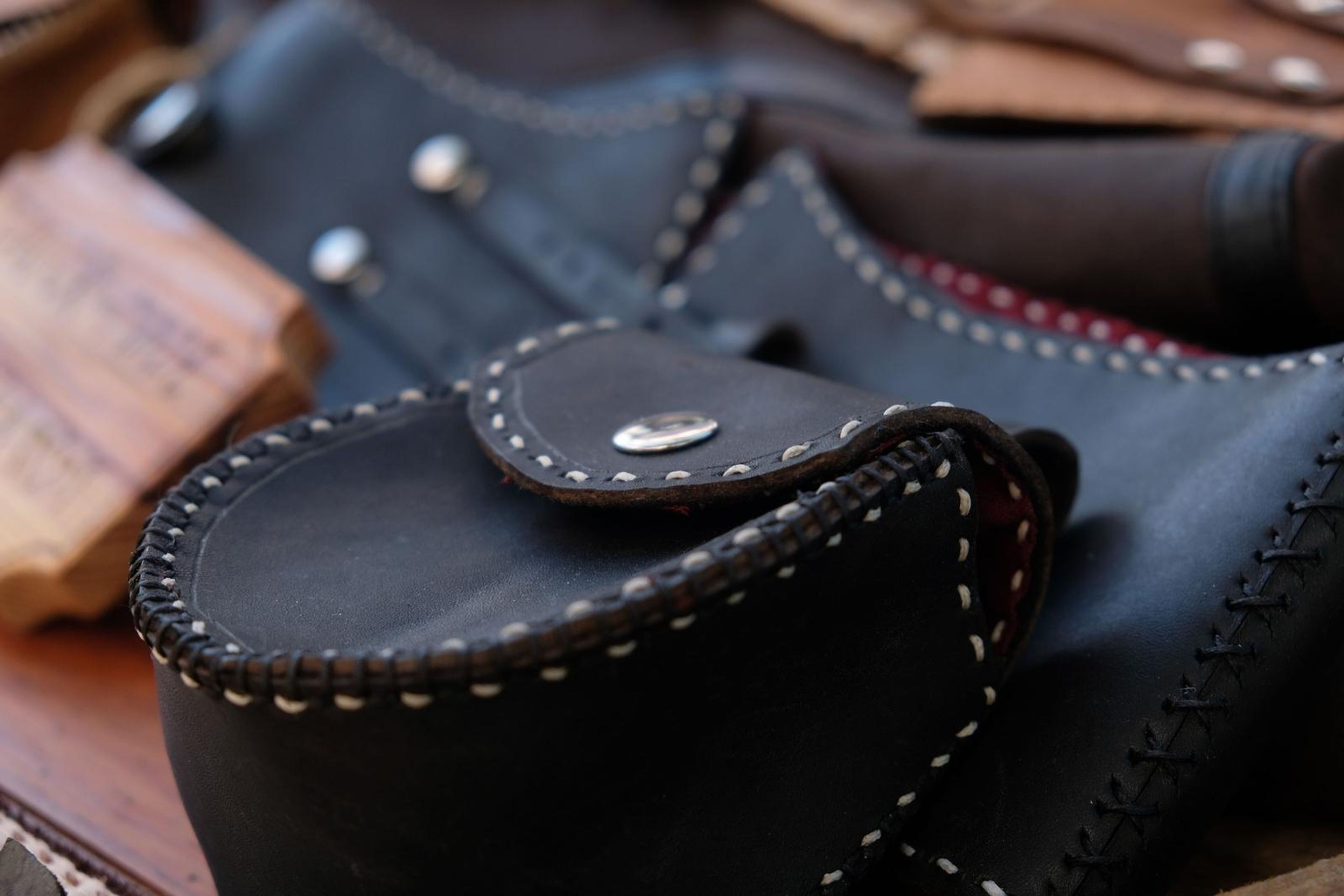 Close-up of a black leather pouch with cream hand-stitched edging and a snap stud