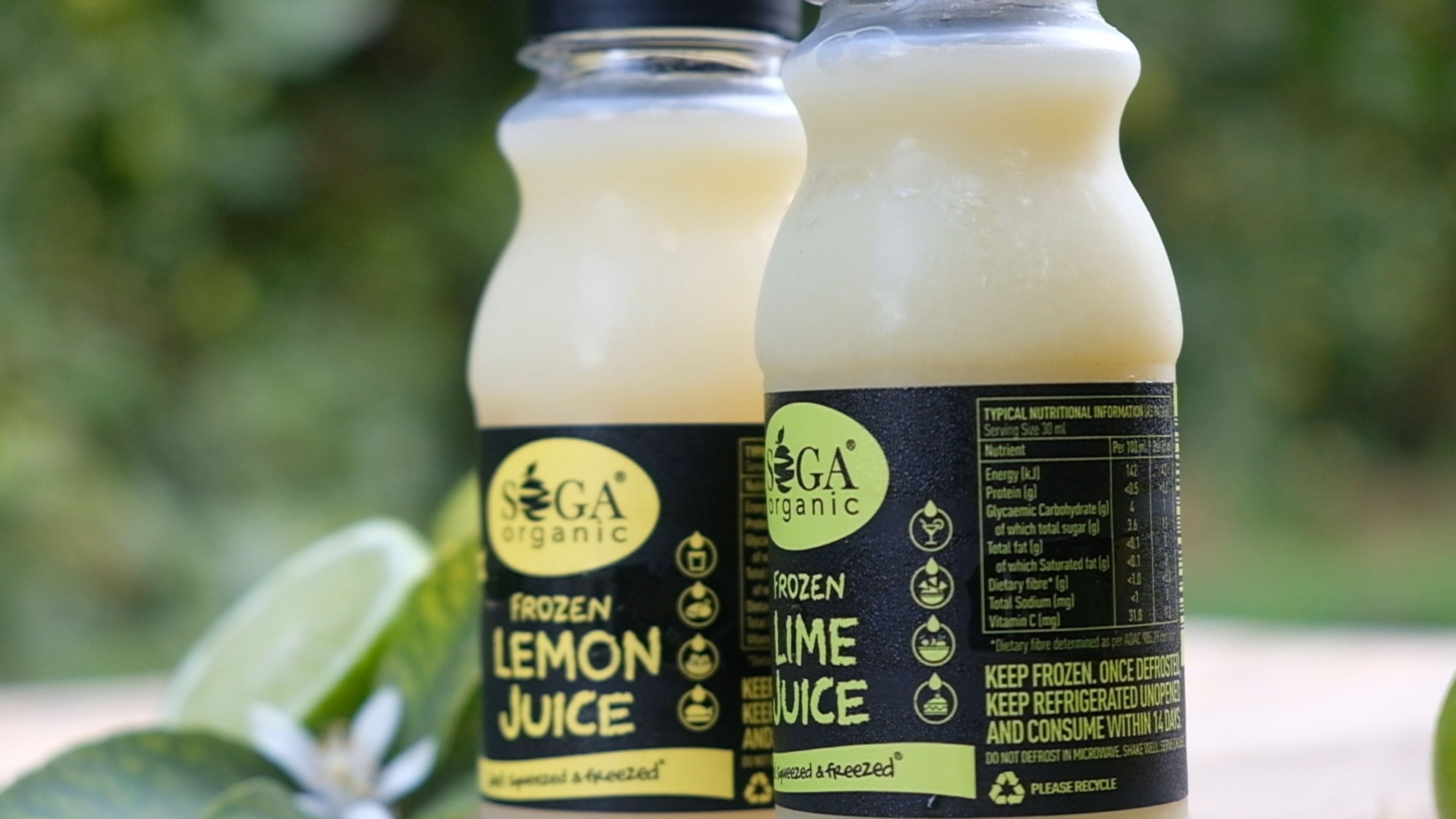 Close-up of SOGA frozen lemon juice and lime juice bottles beside a lime half
