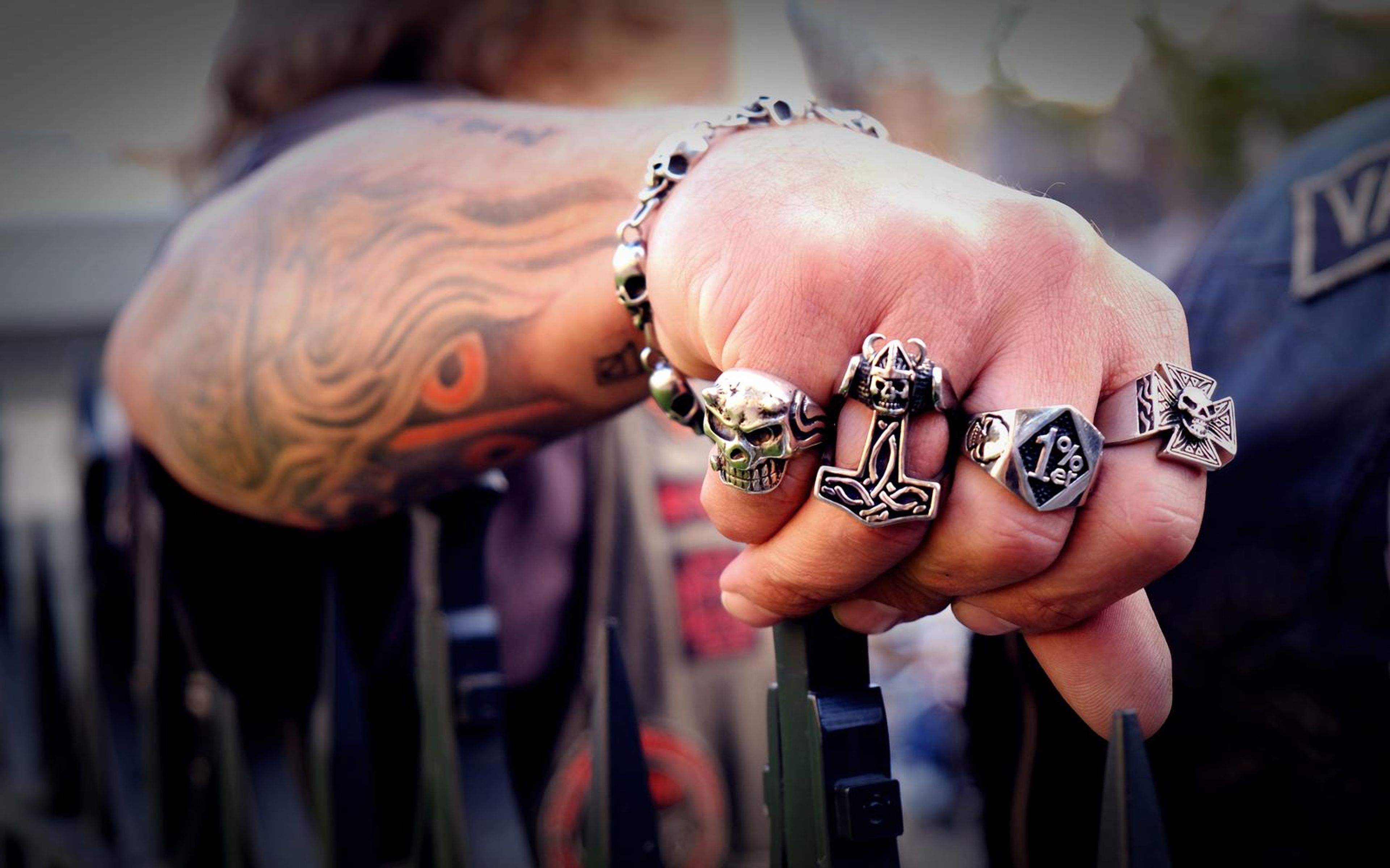 Tattooed forearm with a skull bracelet and a ringed hand in soft focus, resting on a metal rail