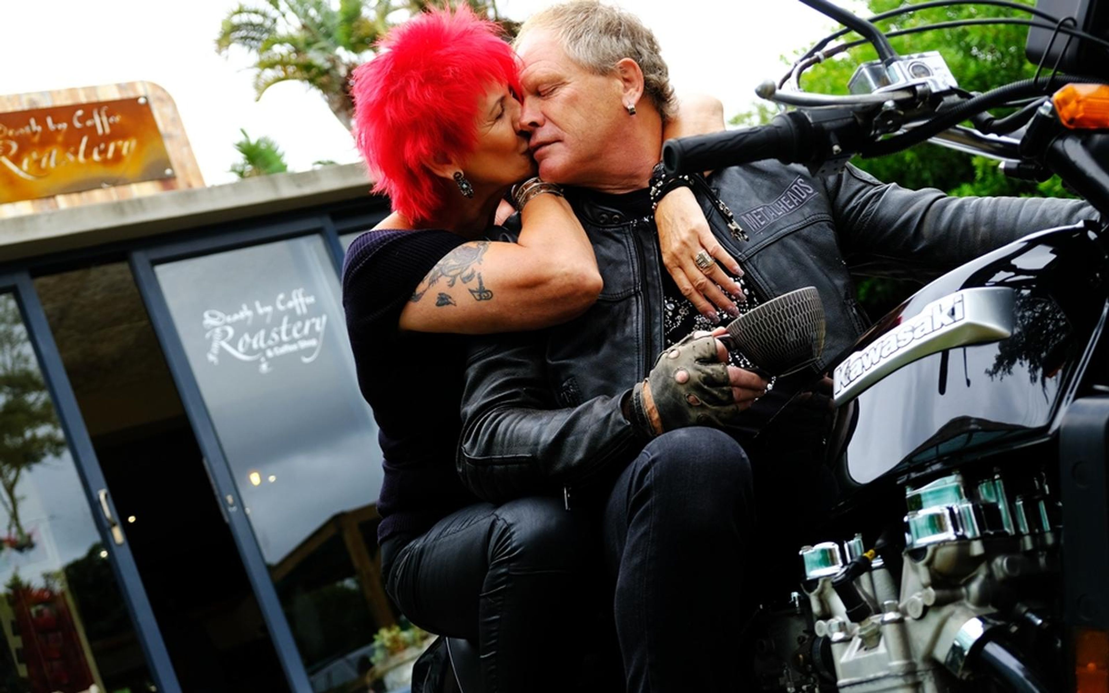 Couple sharing a close moment on a motorbike, woman with red hair nuzzling a man in a black leather jacket