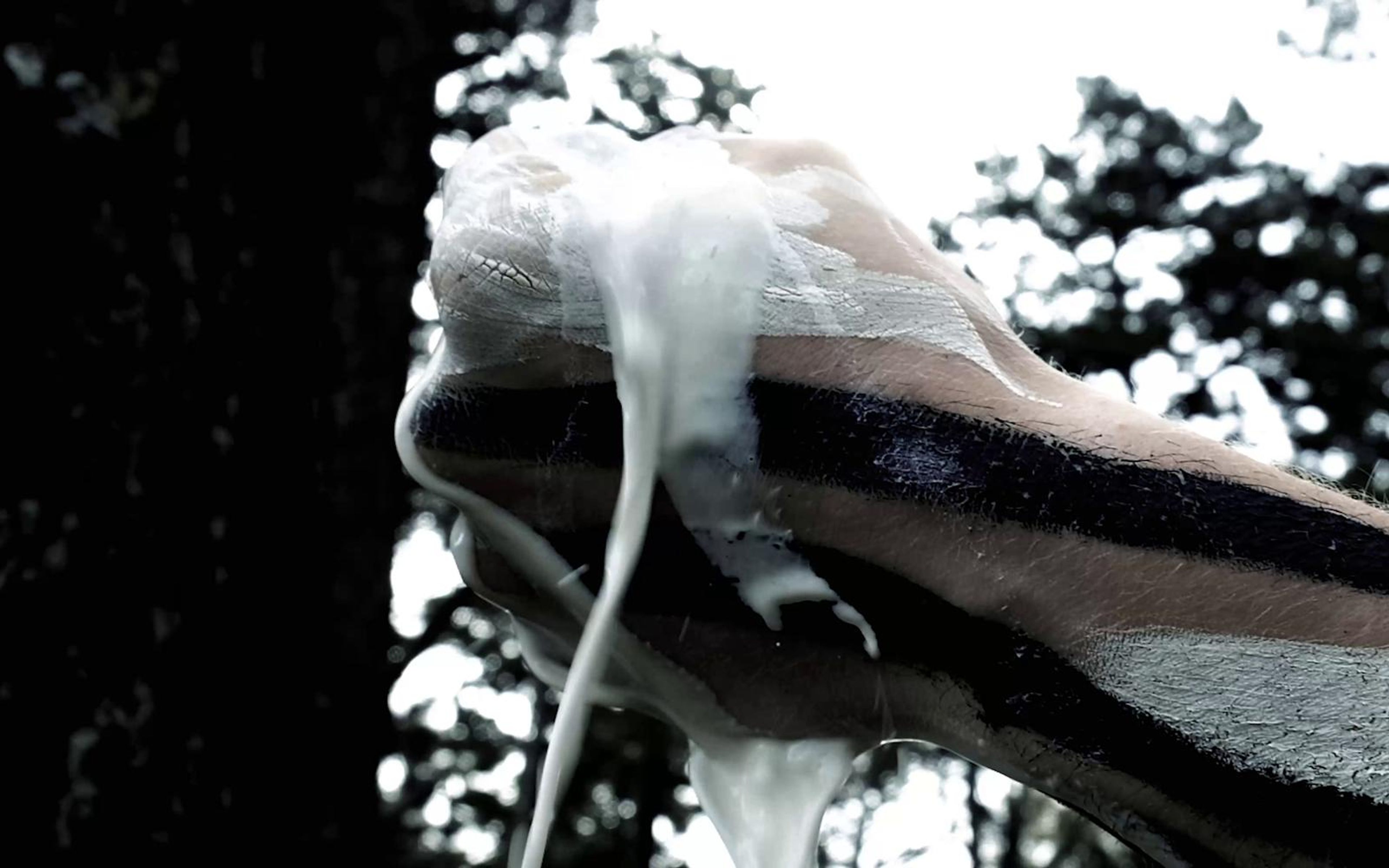 White liquid pouring over a dark painted object against a pale sky
