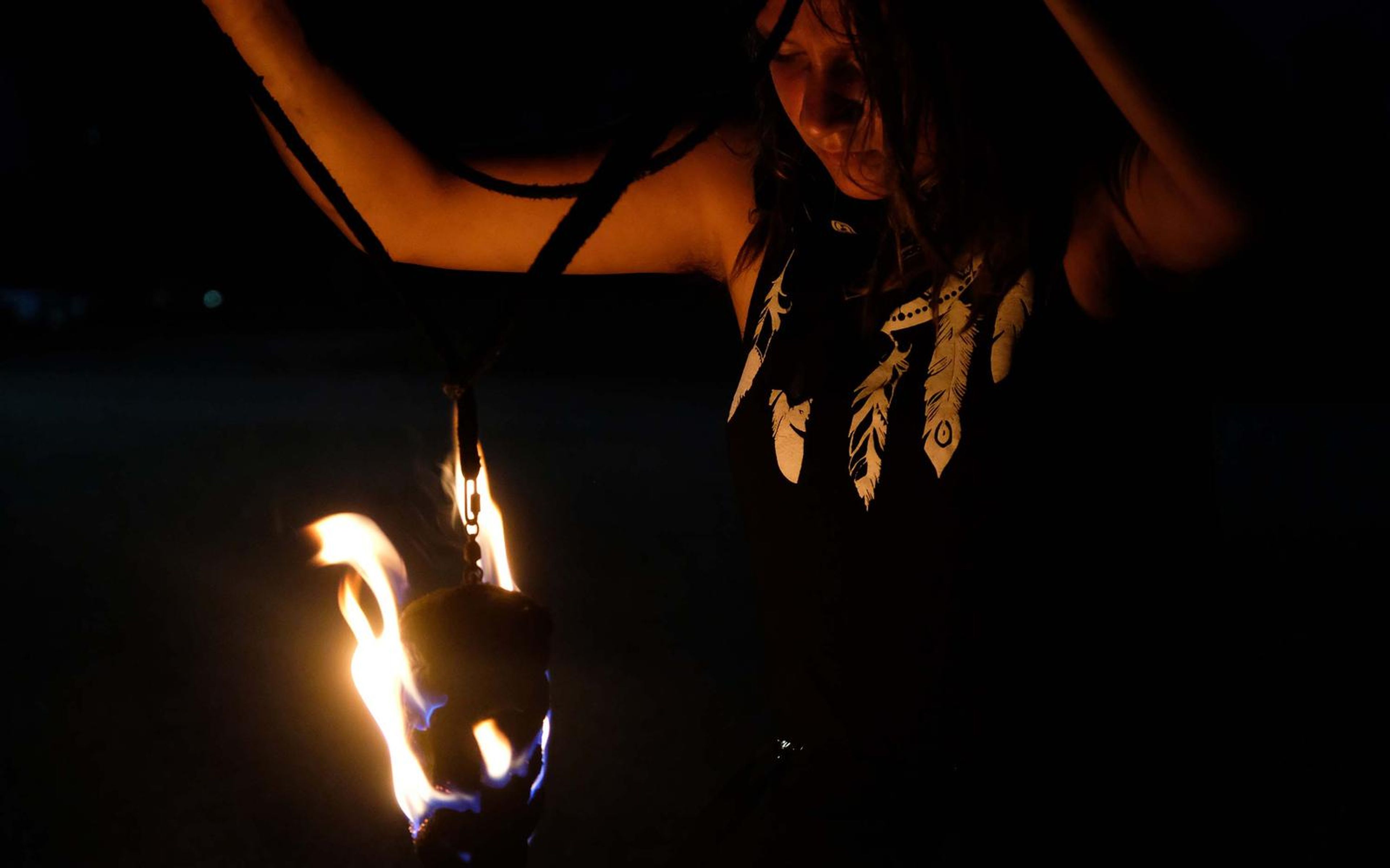 Performer with arms up and a flame burning low at the left, feather print on the top