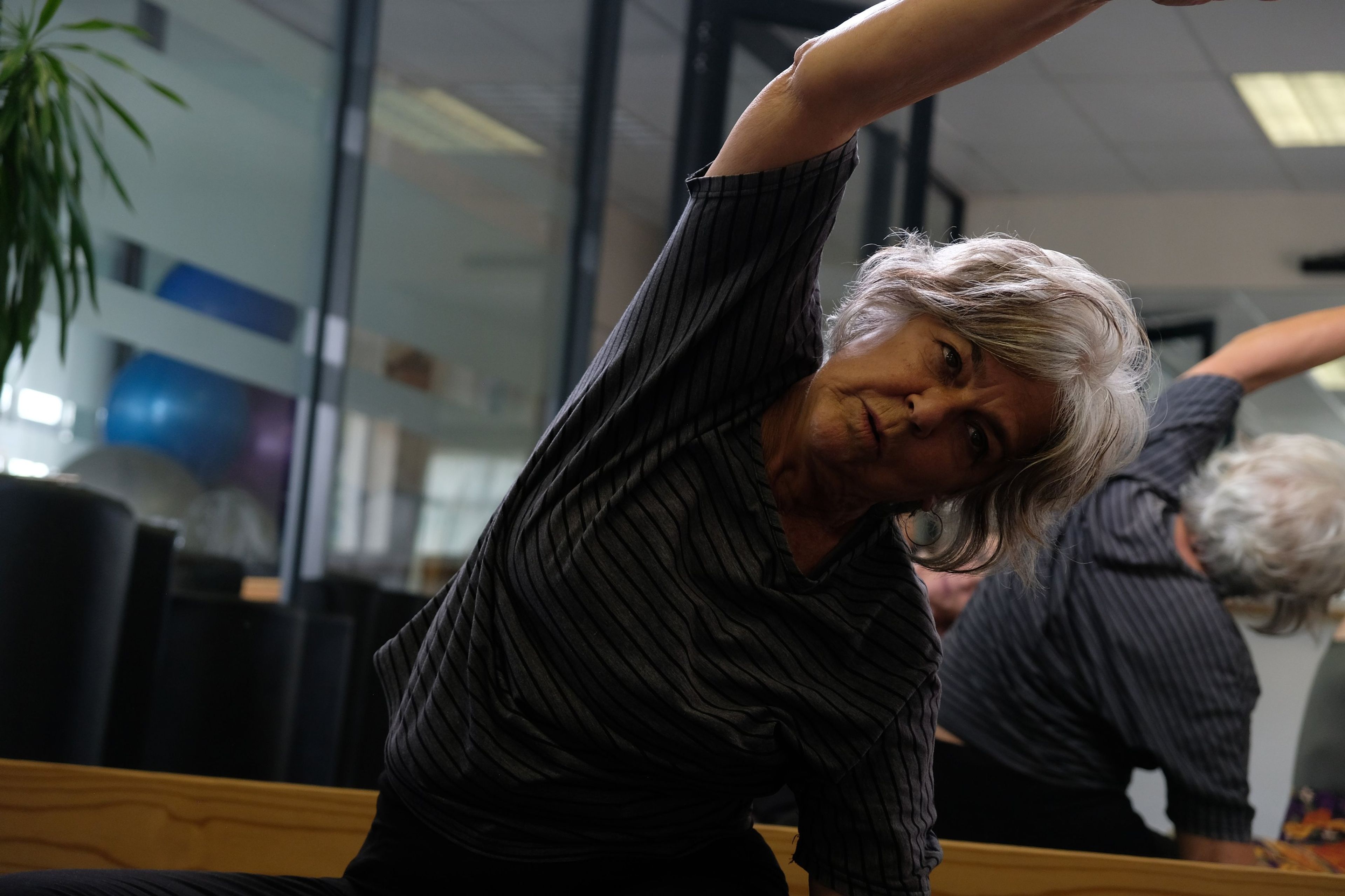 Older instructor in a striped top leaning into a side stretch during a group class