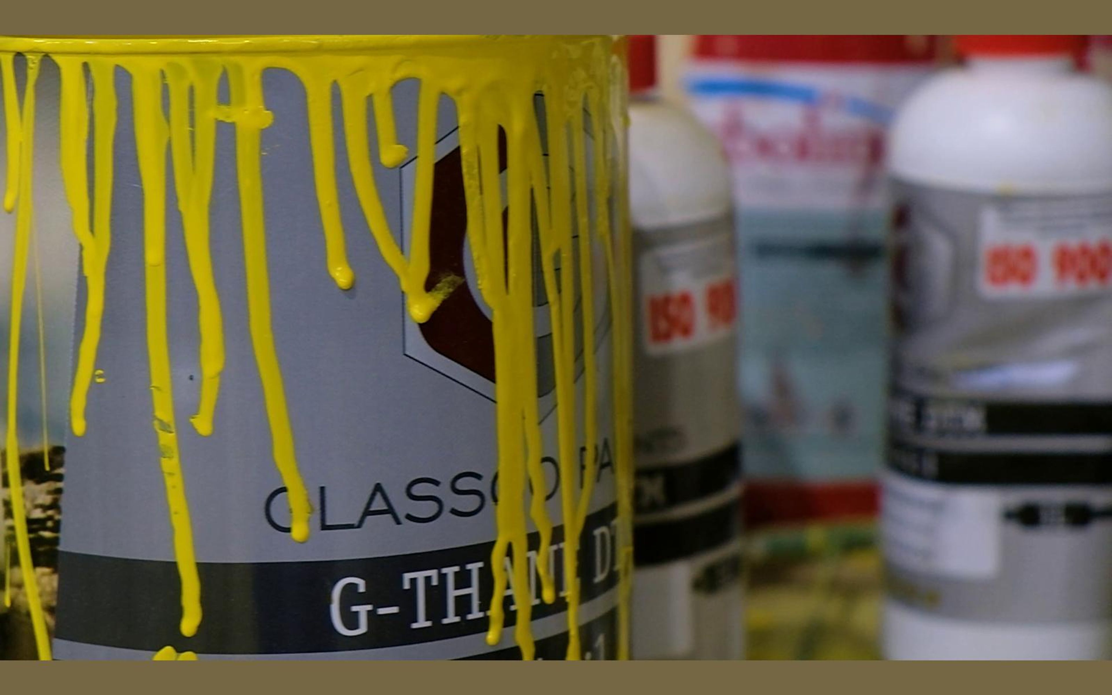 Tin of yellow paint with thick drips beside bottles of thinner