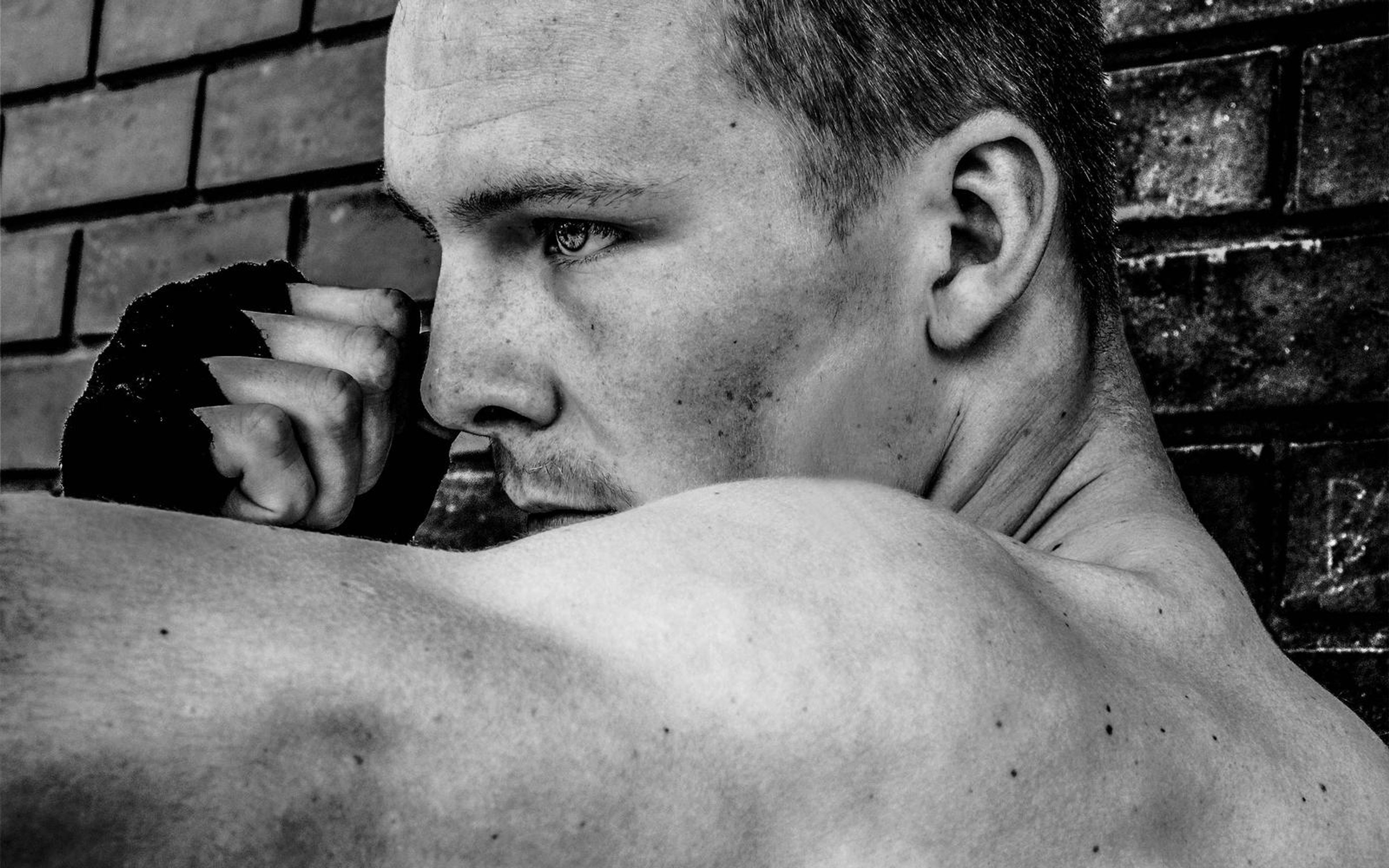 Black and white profile of a man looking sideways with a raised wrapped hand, shoulder in the foreground