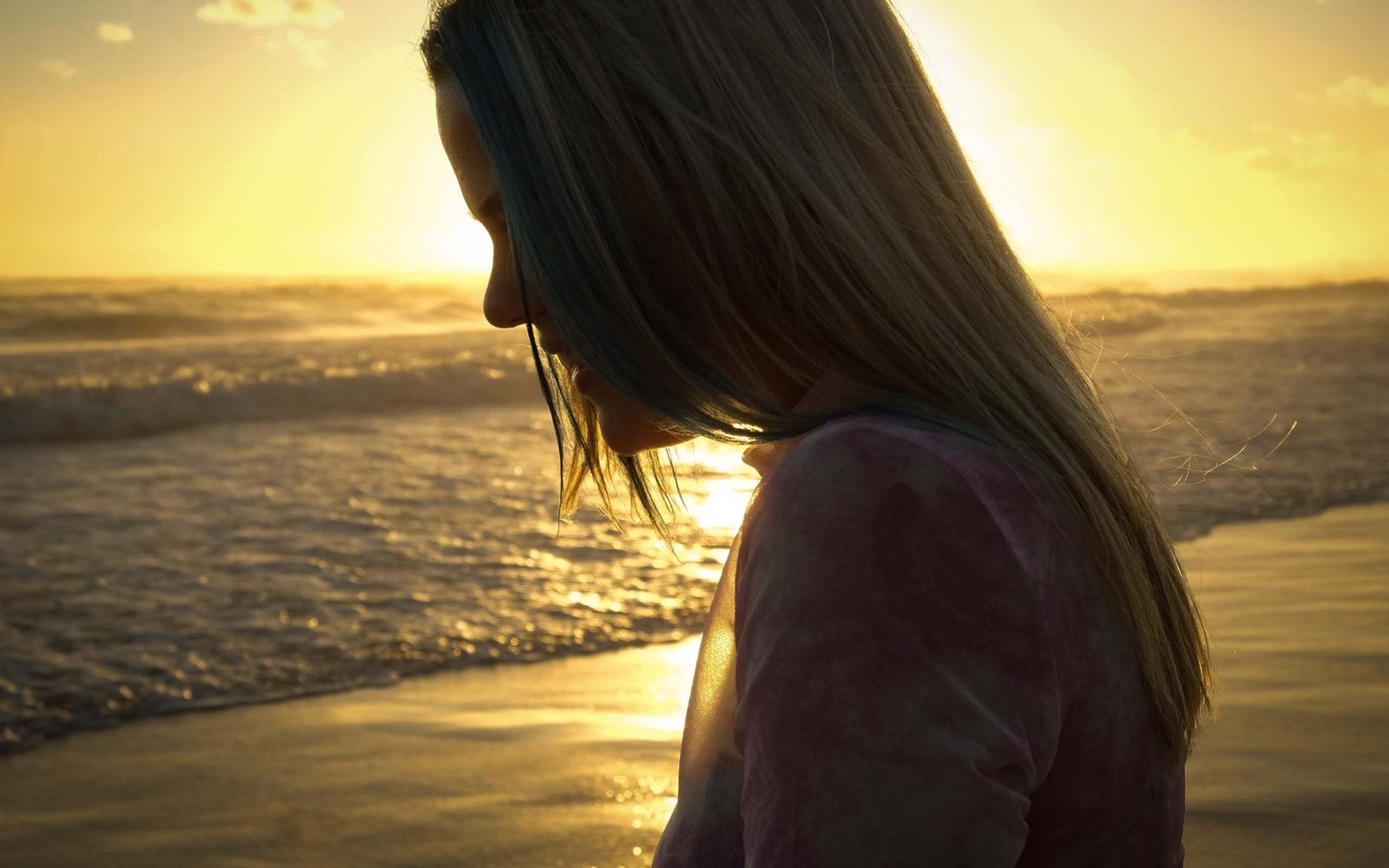 Profile silhouette of a woman with long hair looking down against golden sunset water