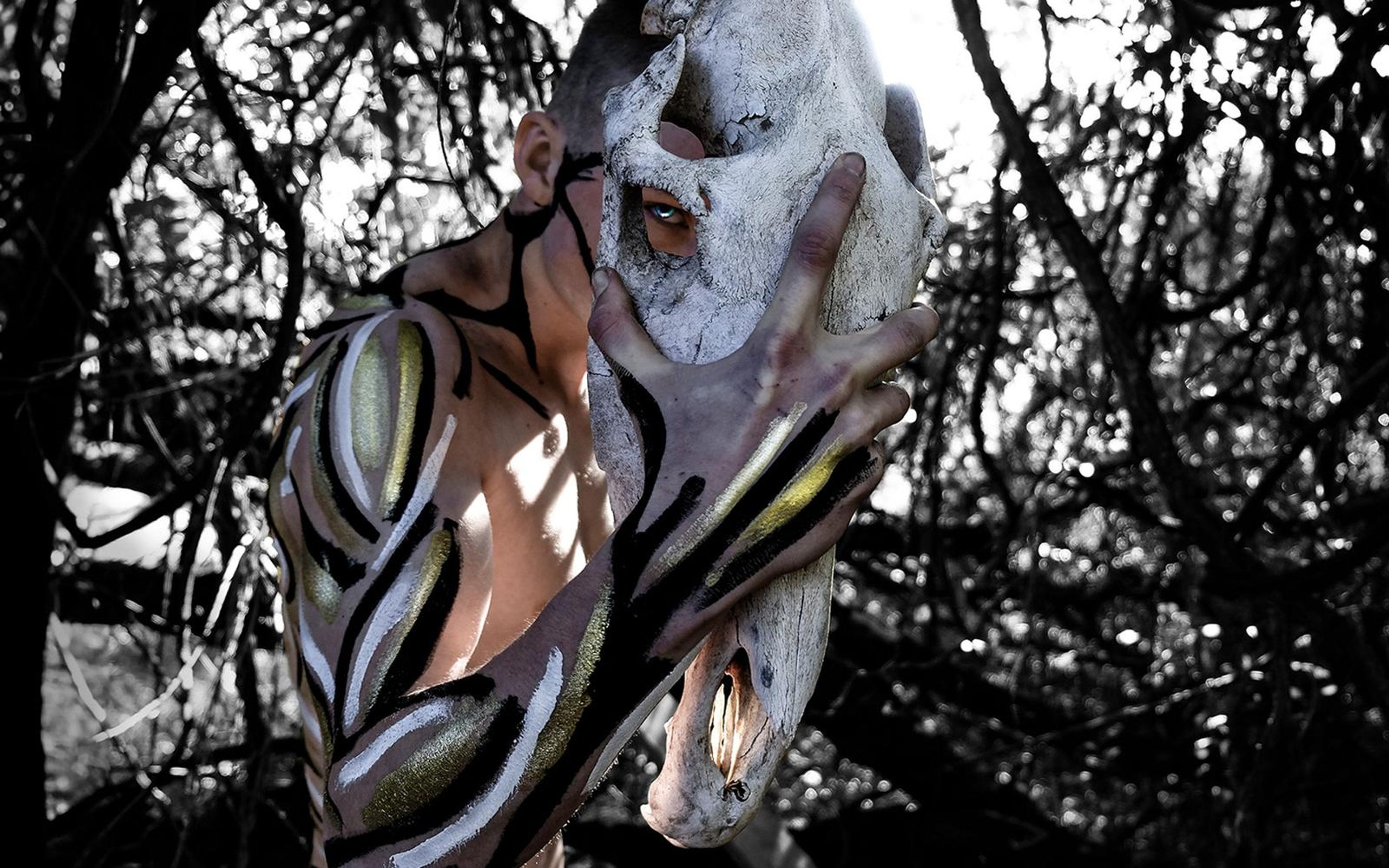 Black and white thicket with a painted performer holding a pale skull against the face, reaching hand with paint patterns