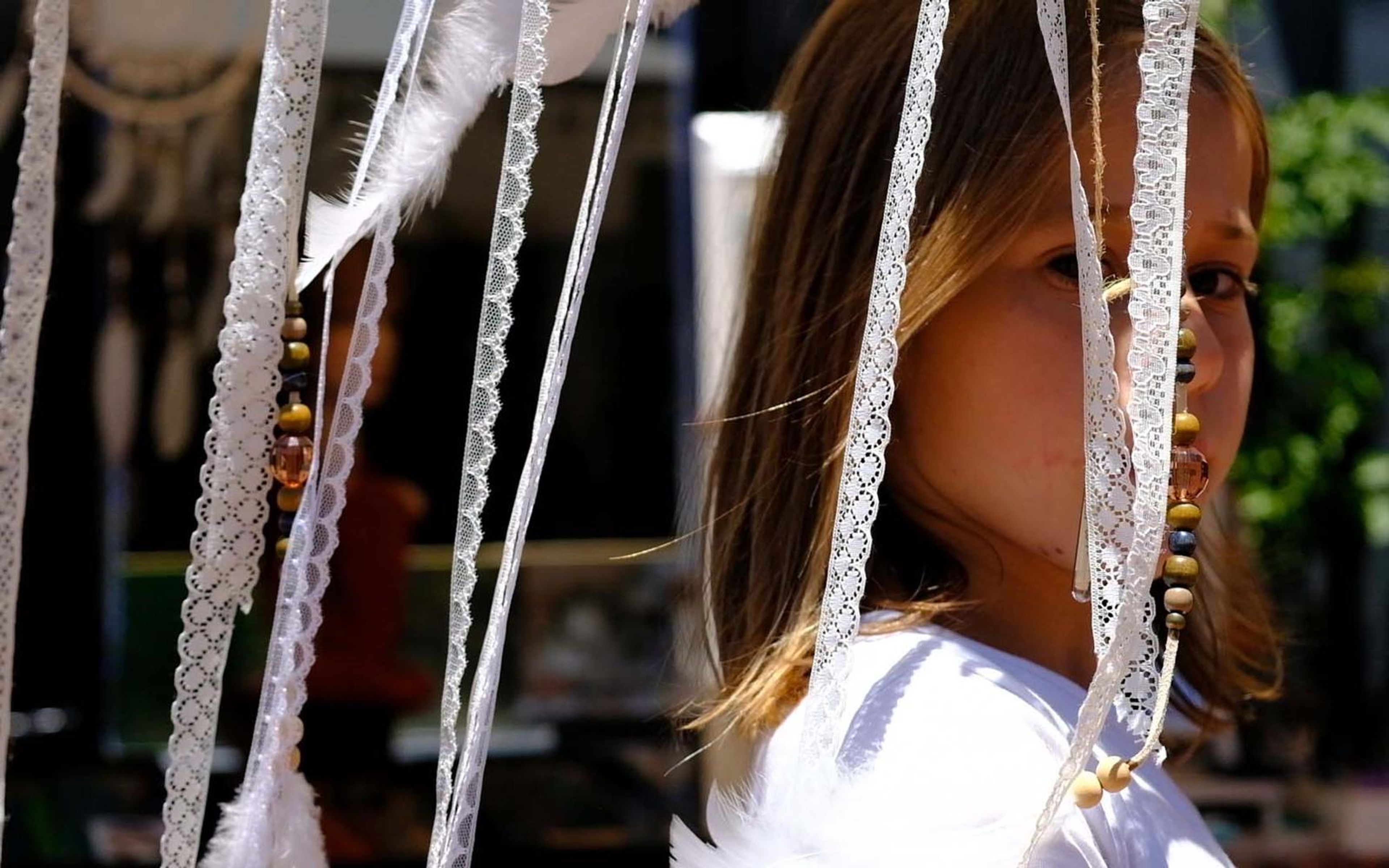 Girl in a white top with long hair seen through hanging lace ribbons and beads