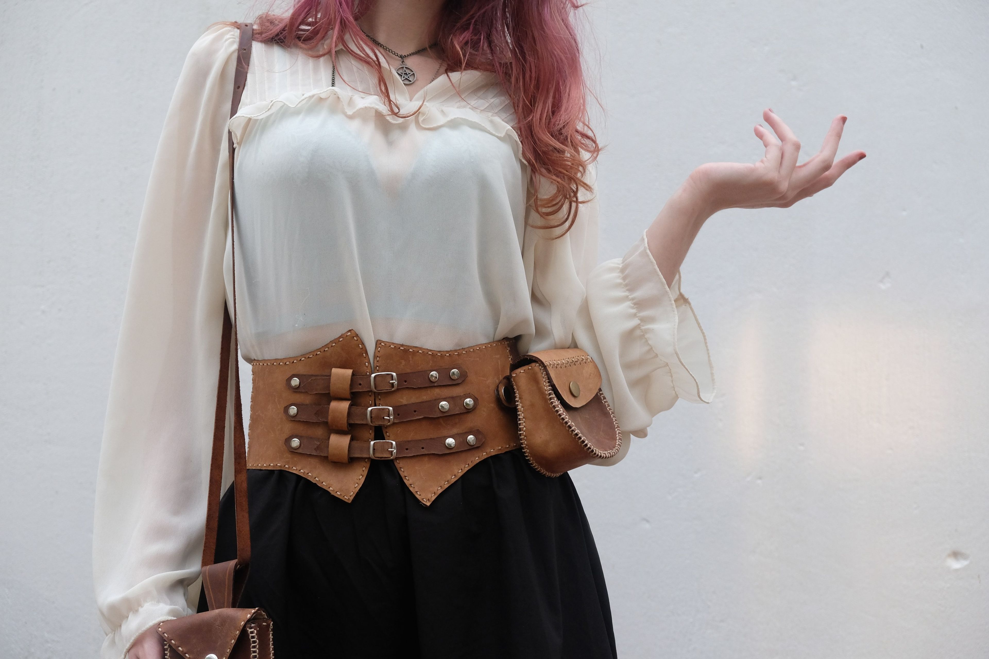 Woman with her hand raised, wearing a leather corset belt and pouch
