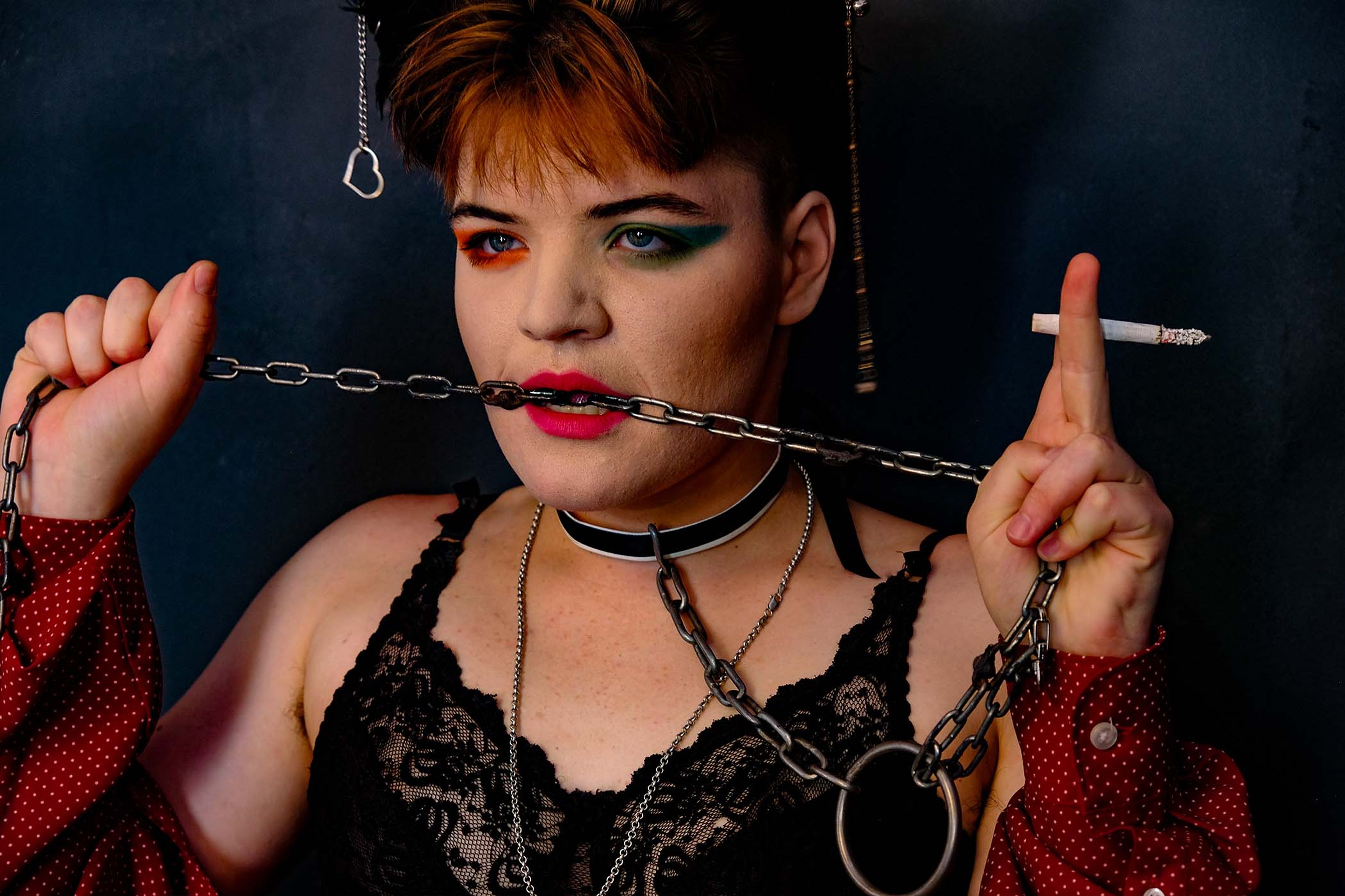 Portrait, subject in a lace bra and chain choker holding a chain between the teeth