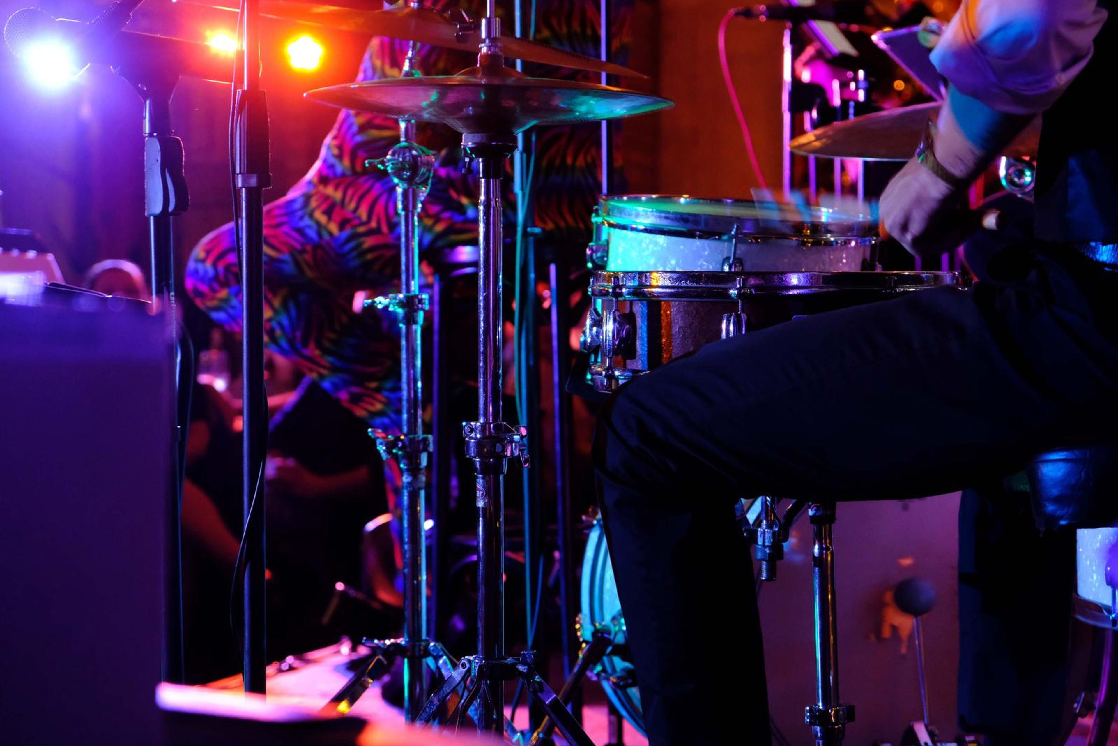 Drummer in rainbow zebra trousers playing under orange stage lights
