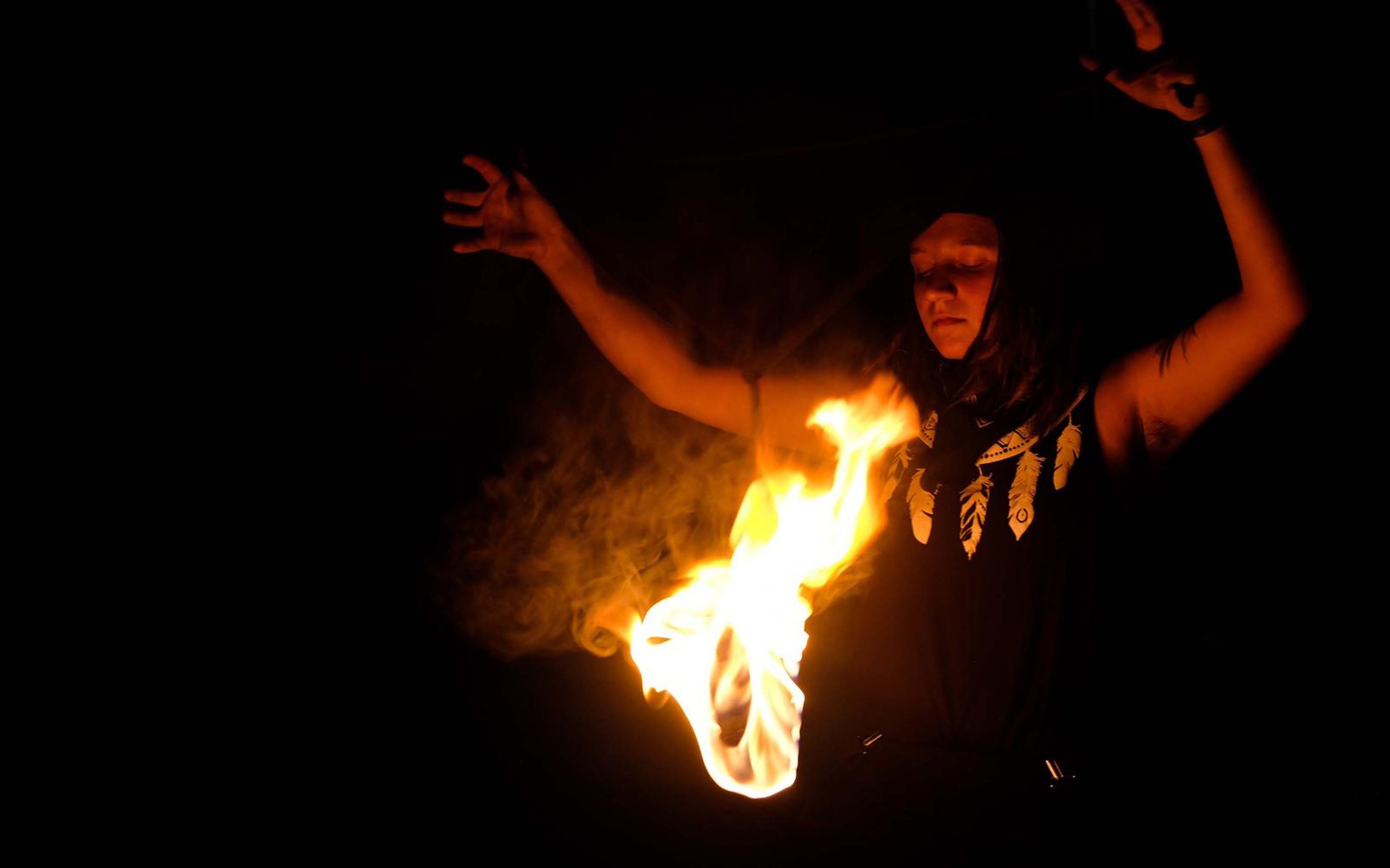 Performer leaning with arms raised and a flame sweeping from the lower left, smoke behind
