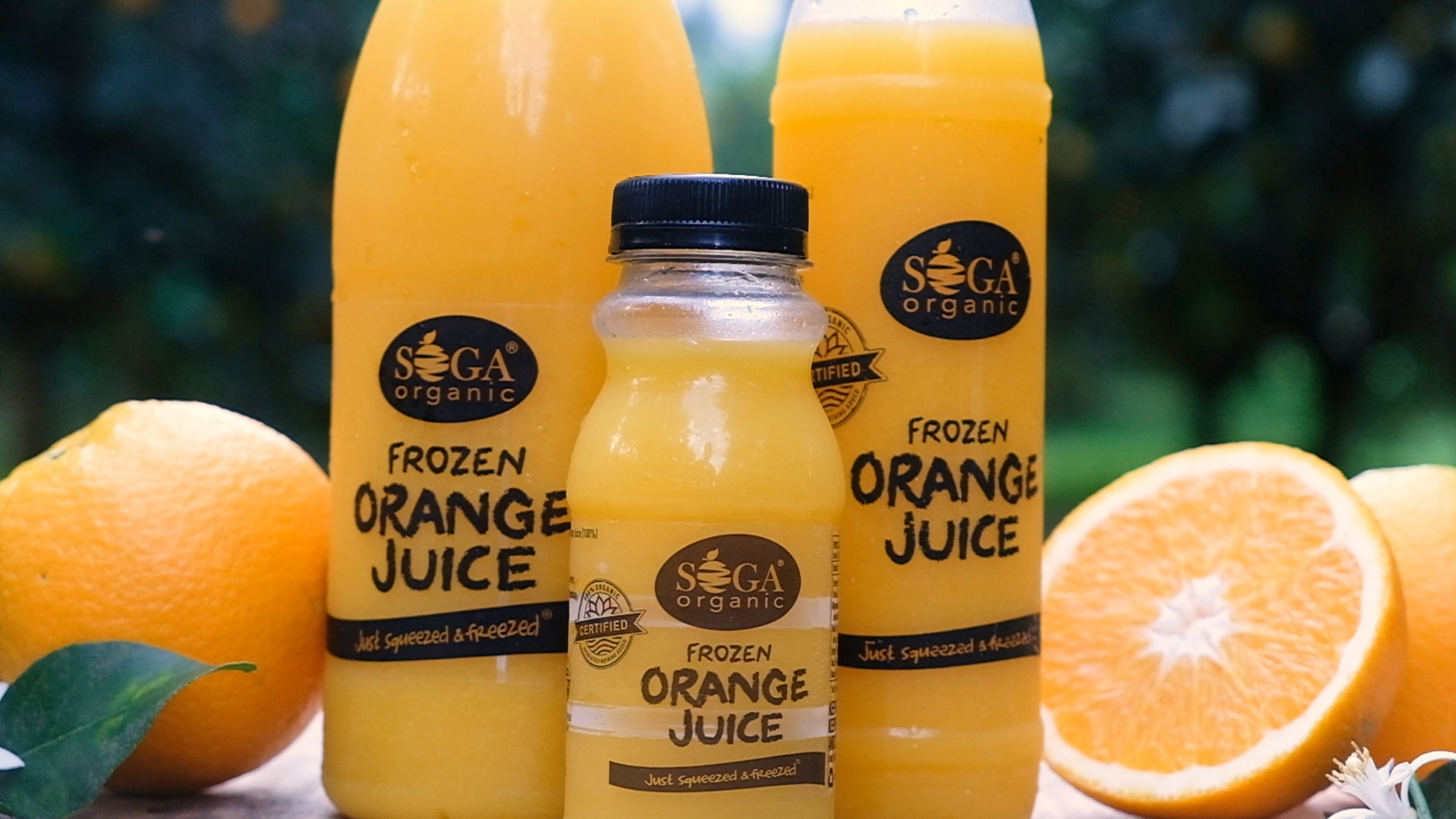 Frozen orange juice bottles beside orange halves and leaves on a wooden table