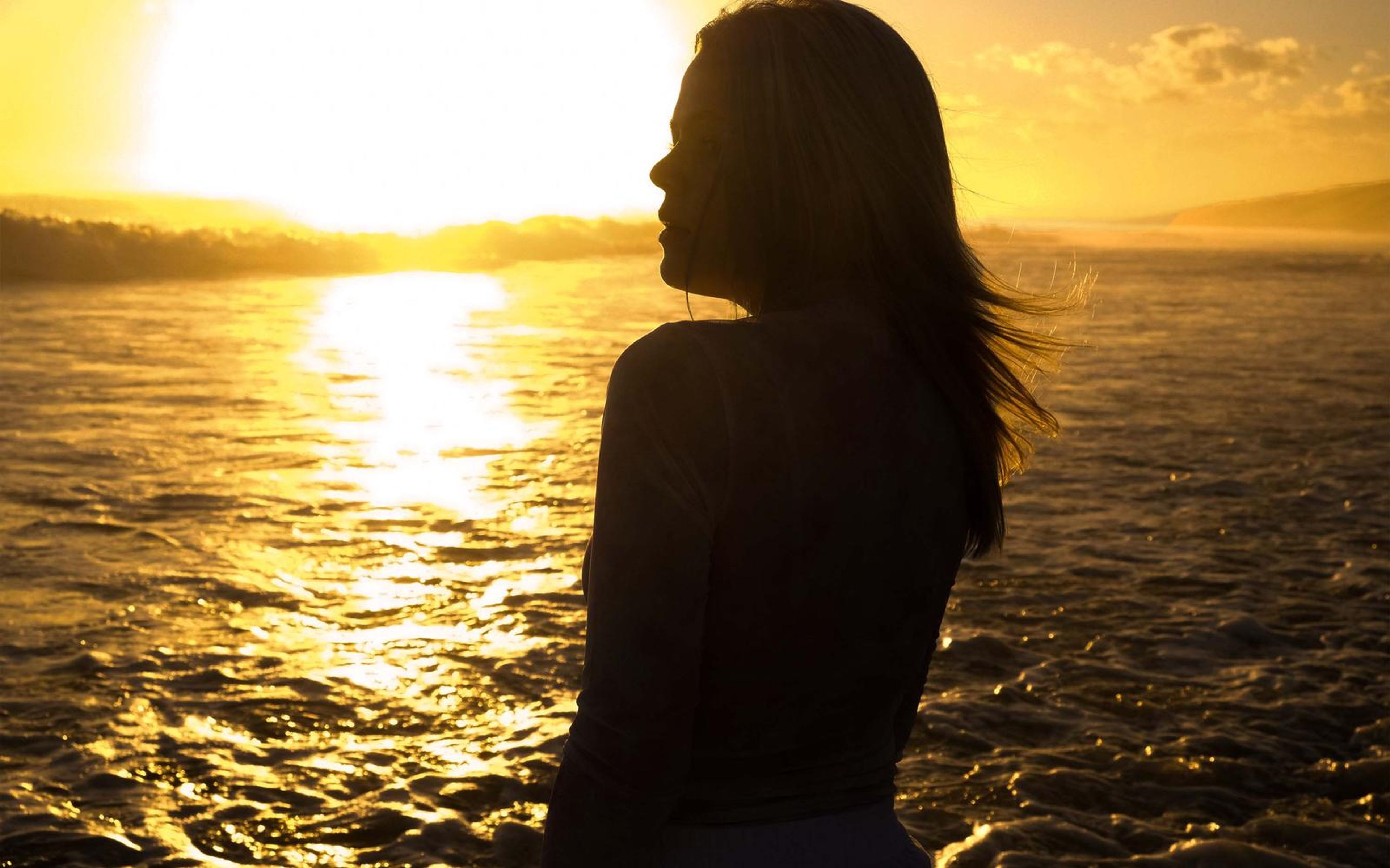 Profile silhouette of a woman with flowing hair against golden sea reflections