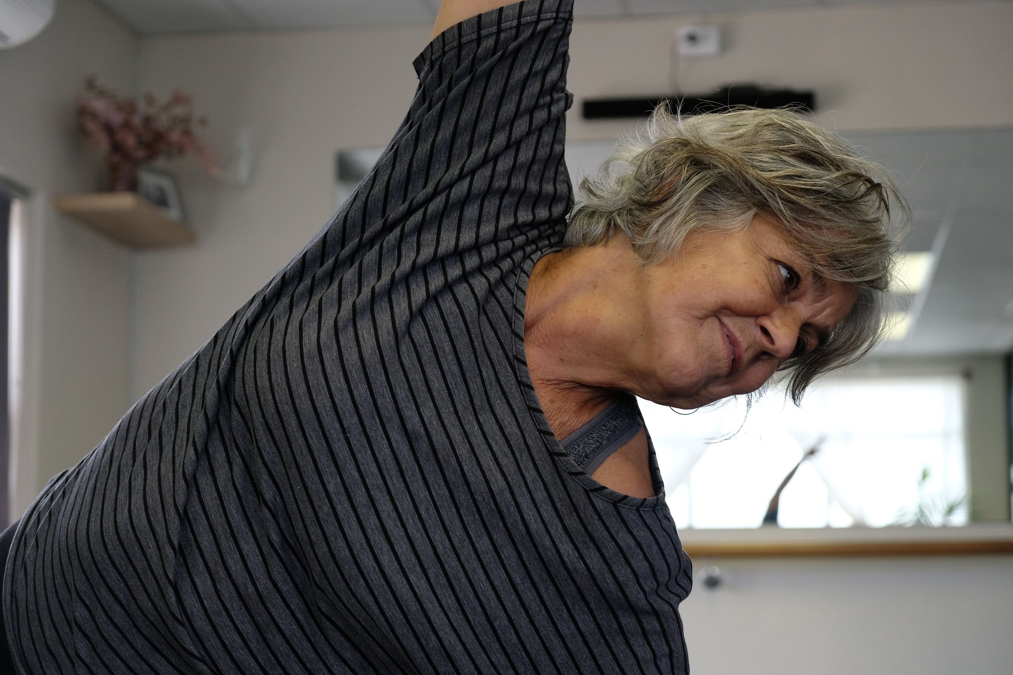 Close view of an older instructor in a striped top leaning into a side stretch
