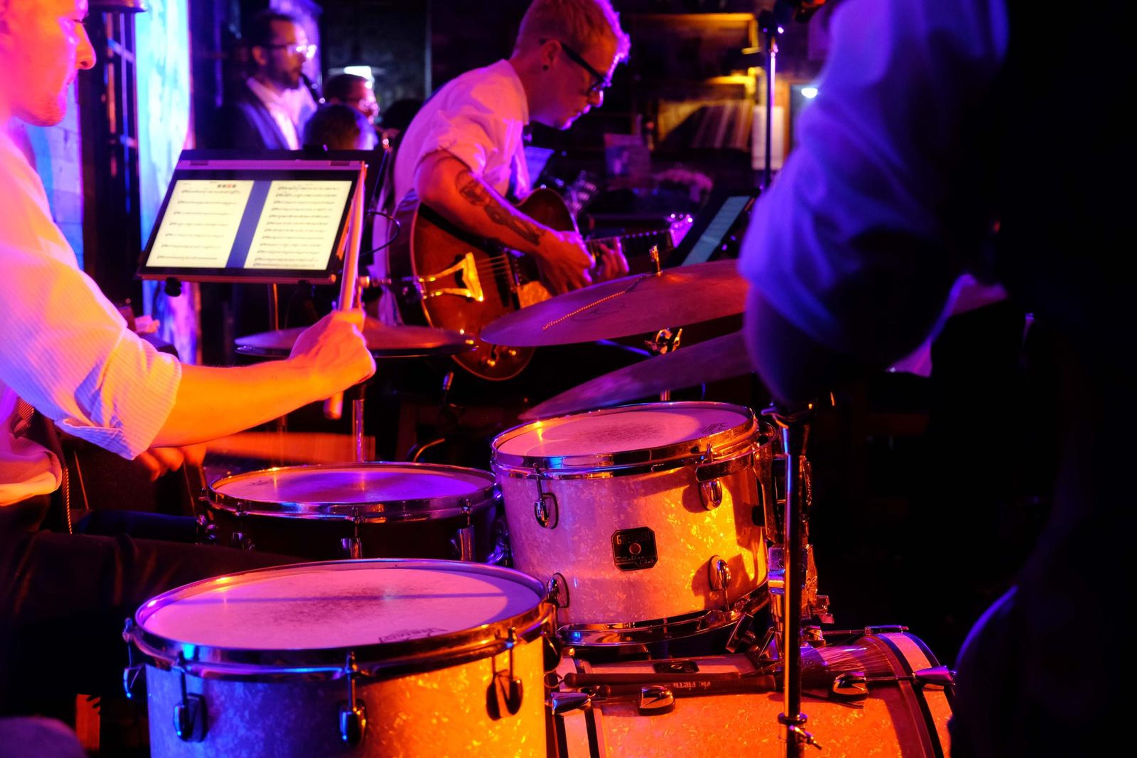 Drummer in action beside a guitarist reading from a tablet