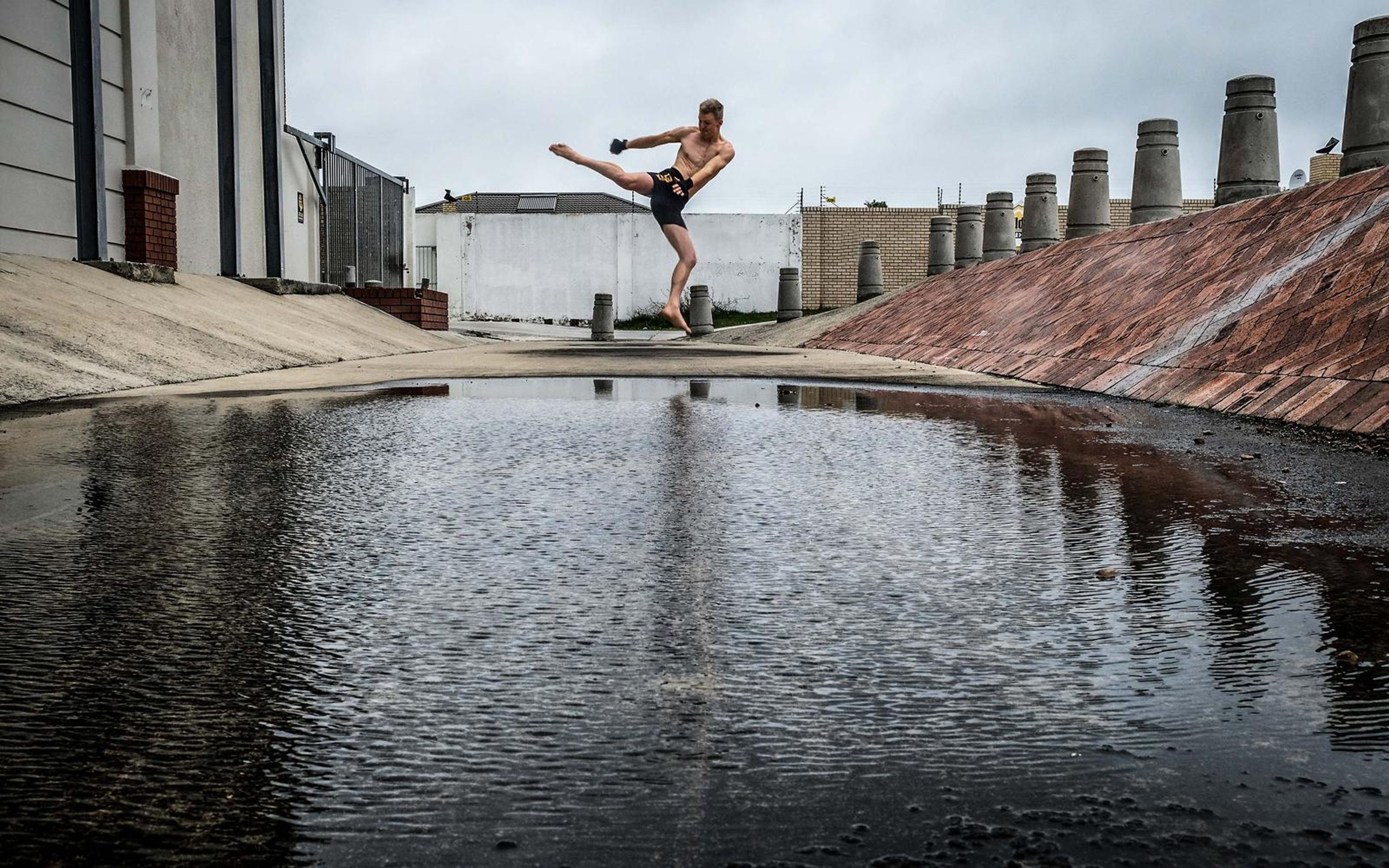 Man mid high kick over a puddle with reflections below, cloudy sky