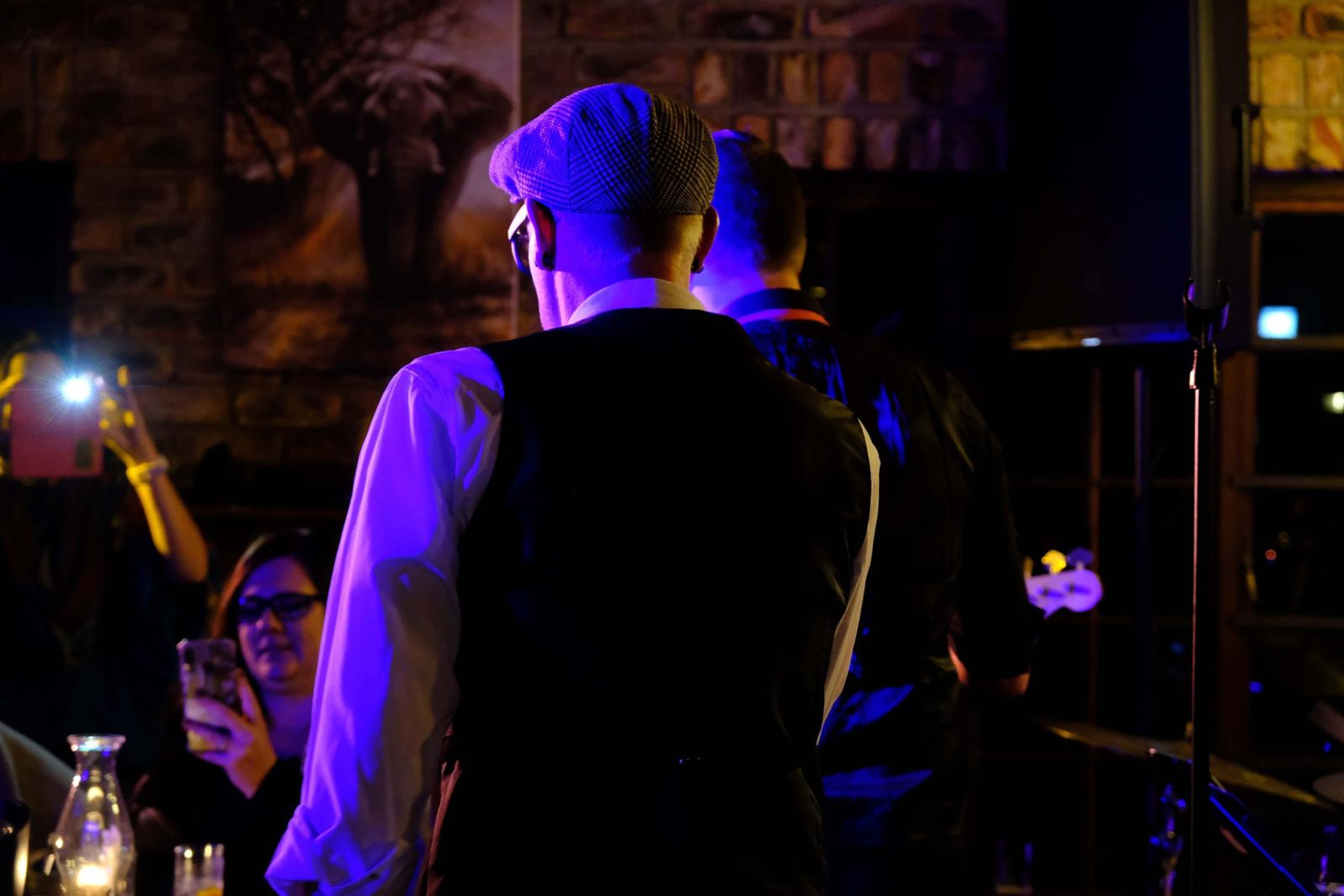 Singer in a flat cap and waistcoat holding a phone torch while he sings
