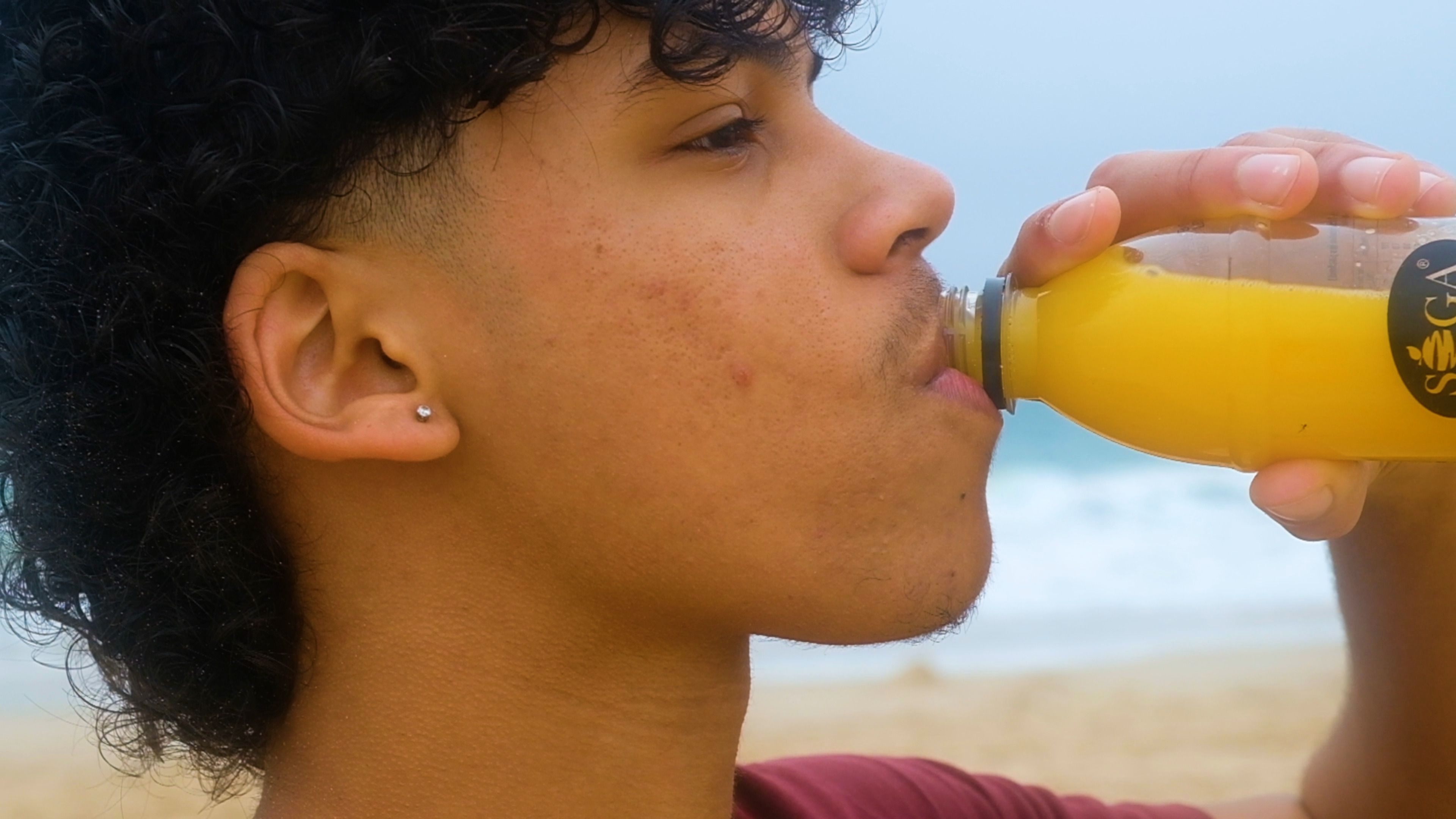 Close-up of a young man taking a drink of orange juice by the sea