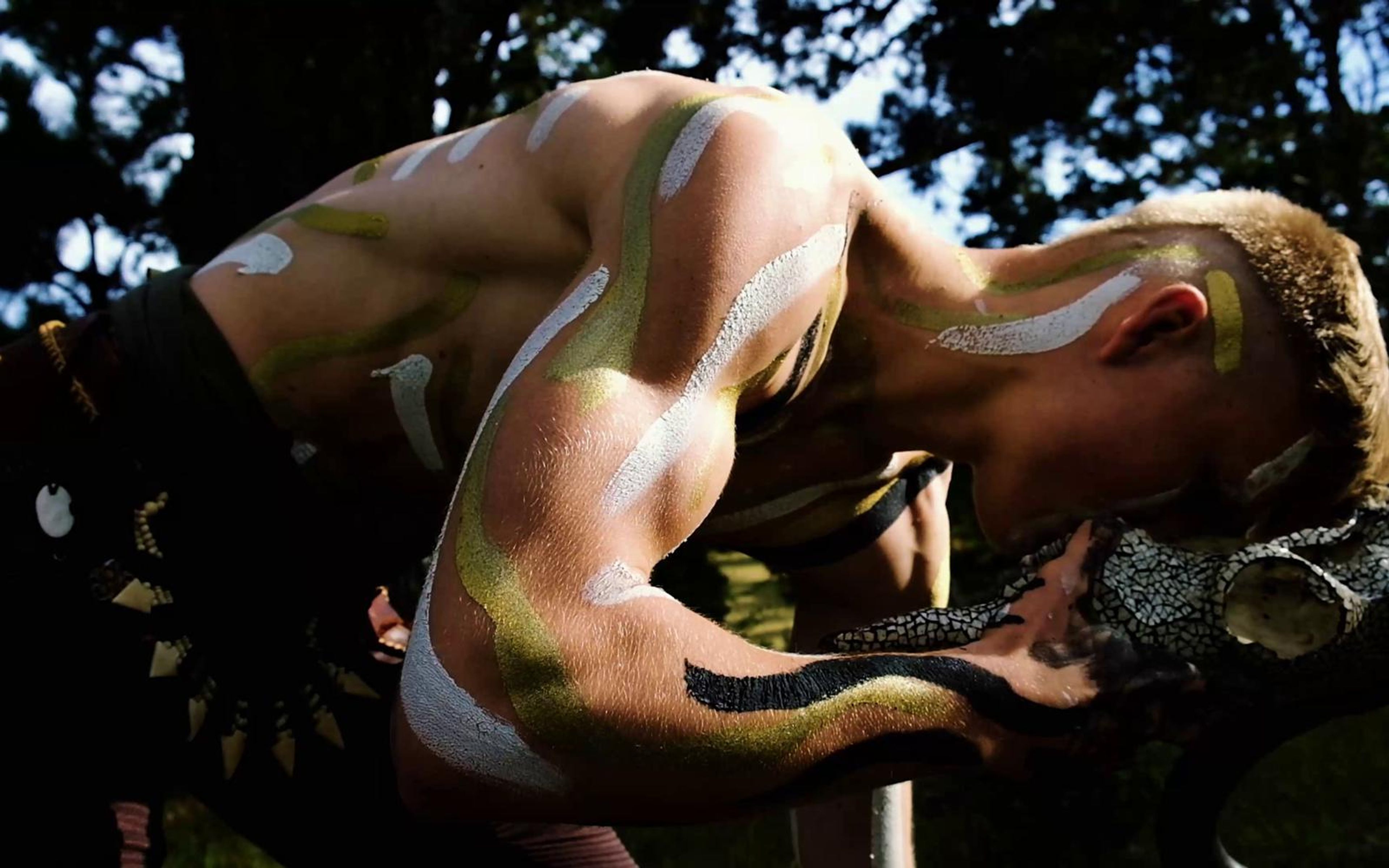 Performer bent forward with painted shoulders holding a mask in a high contrast grade
